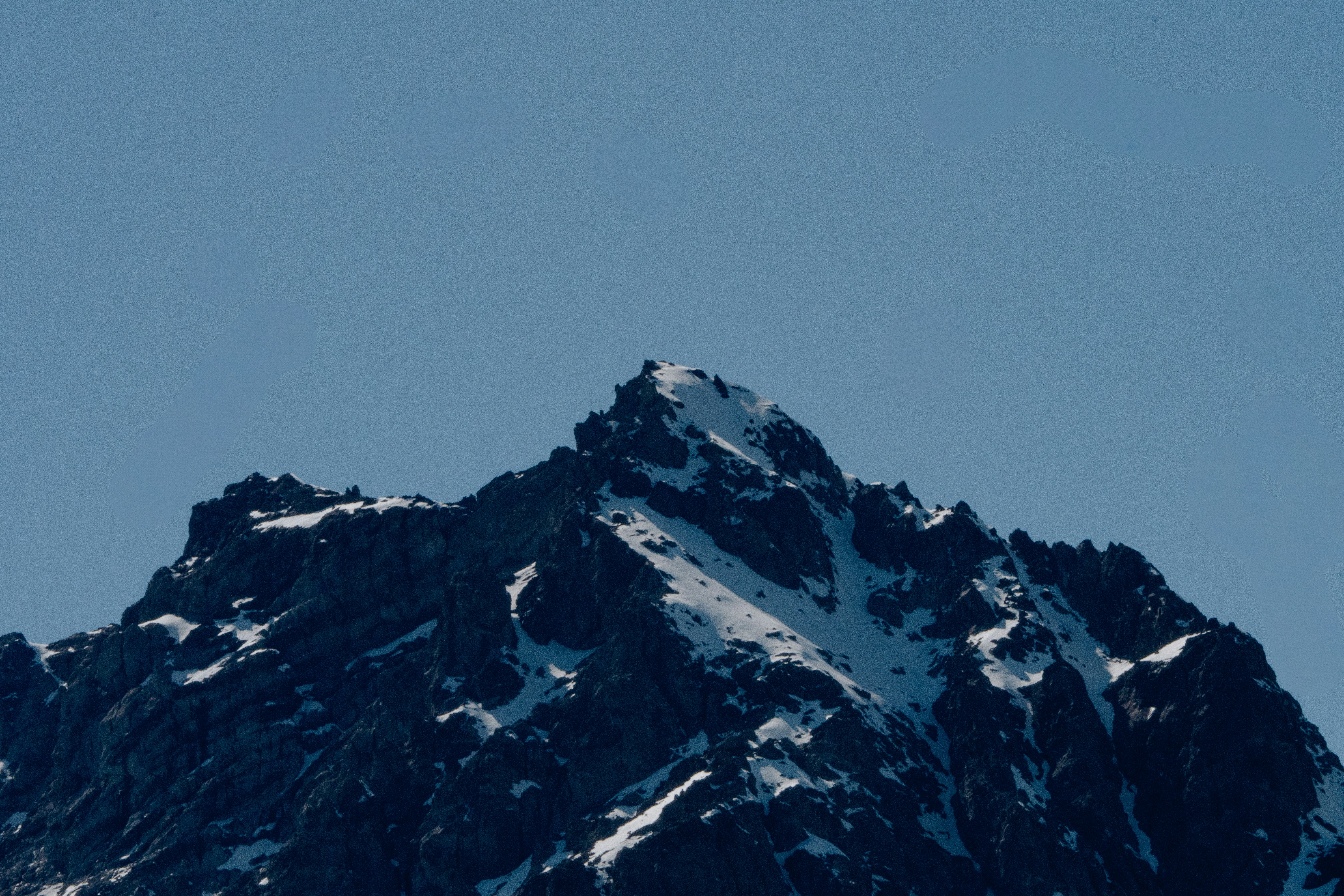 A jagged mountain peak with patches of snow against a clear blue sky