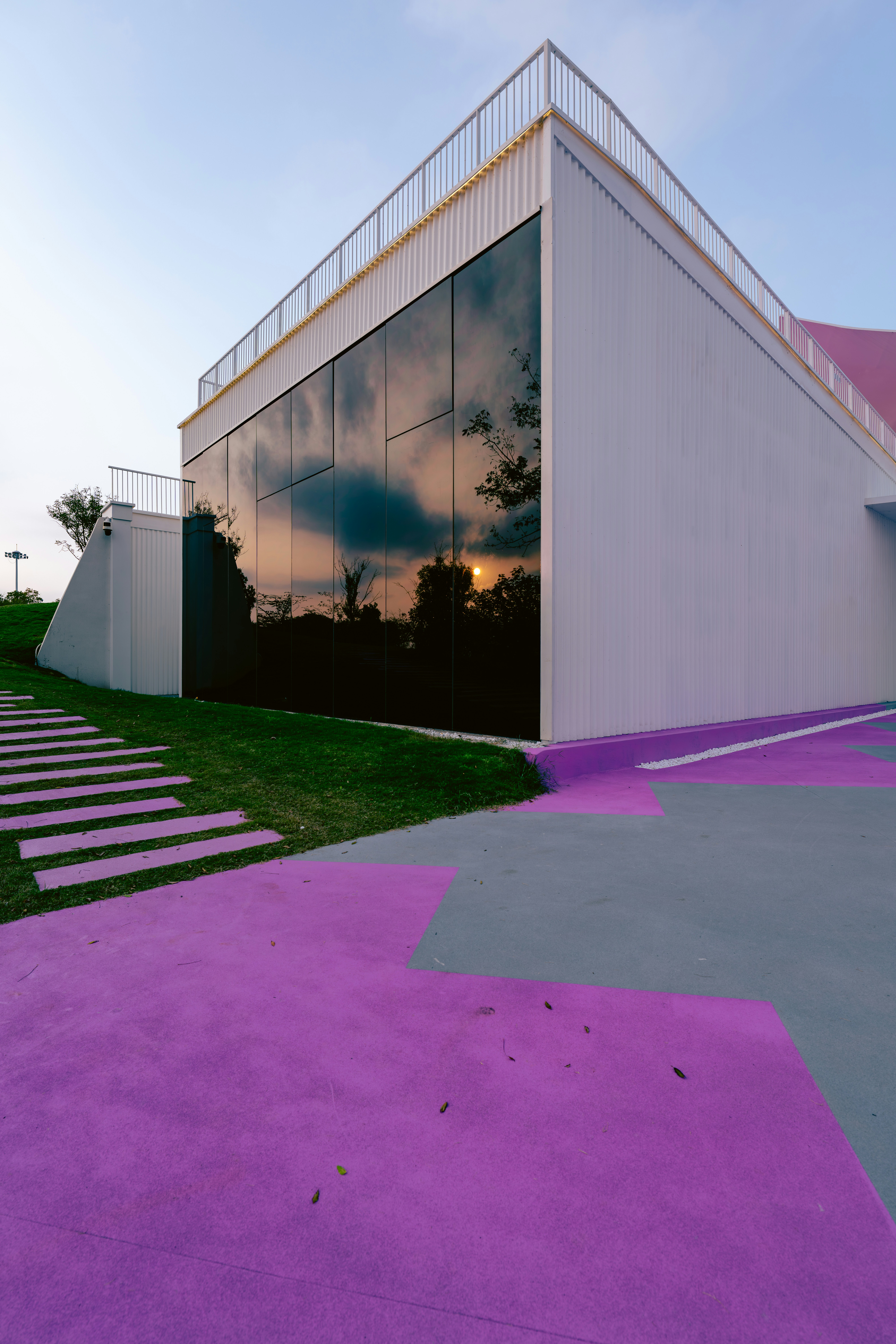 Edificio moderno con paredes de cristal reflectante que reflejan un sol bajo y árboles