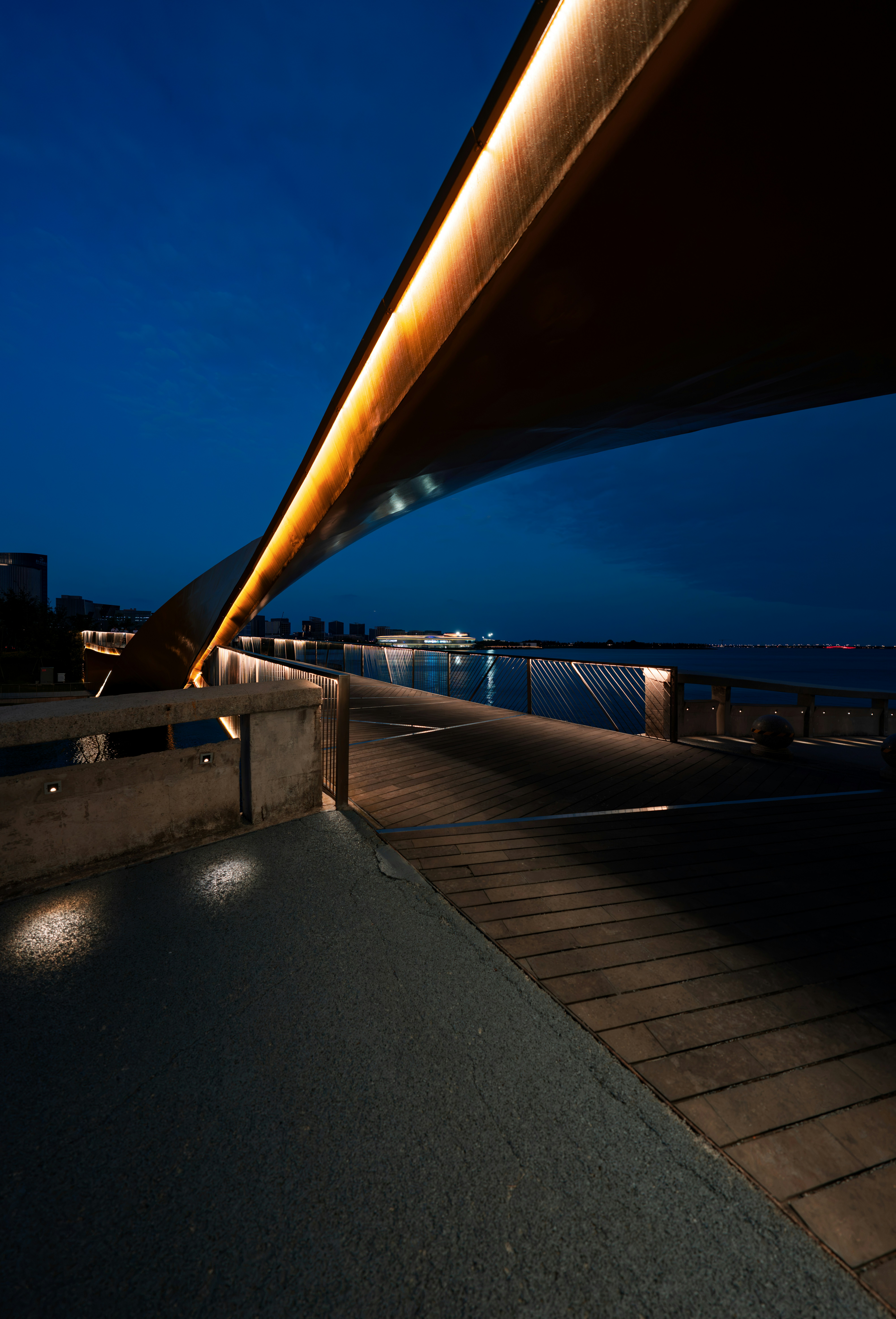 Un puente peatonal moderno con iluminación cálida sobre un cuerpo de agua oscuro