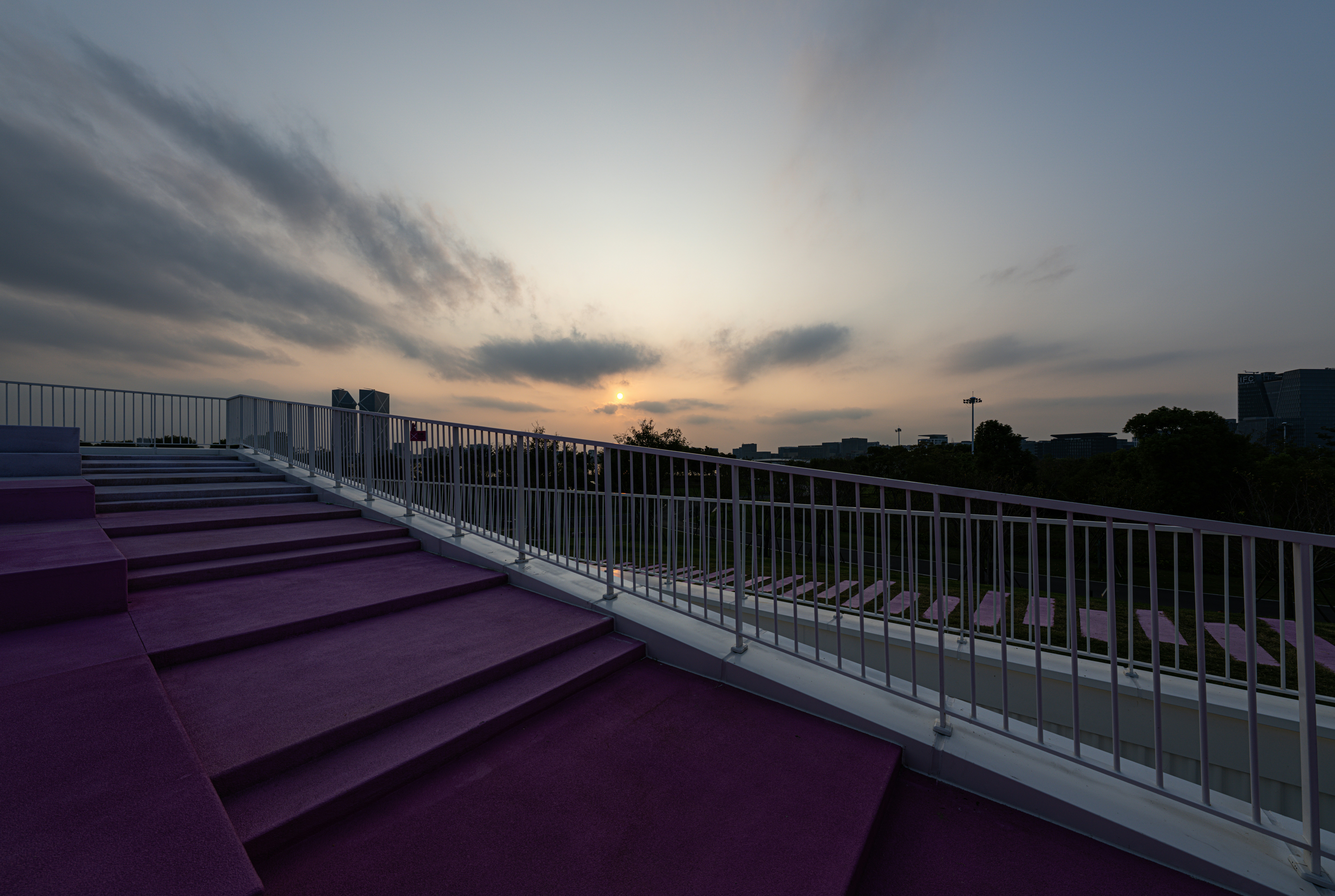 Escaleras moradas con barandillas blancas que conducen hacia el horizonte de una ciudad bajo un cielo brumoso
