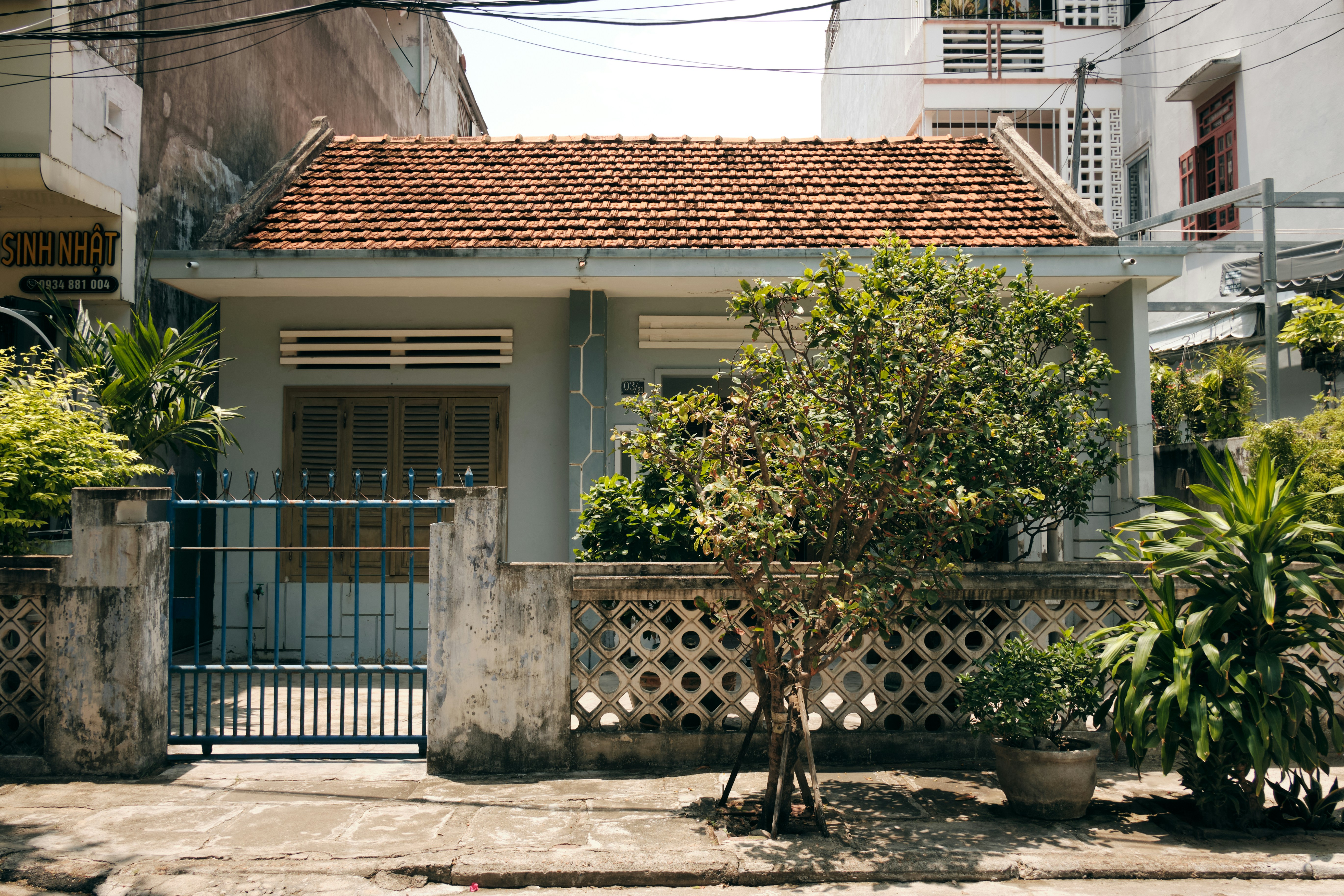 Rumah lama beratap genteng tanah liat di balik pagar tembok dan gerbang biru