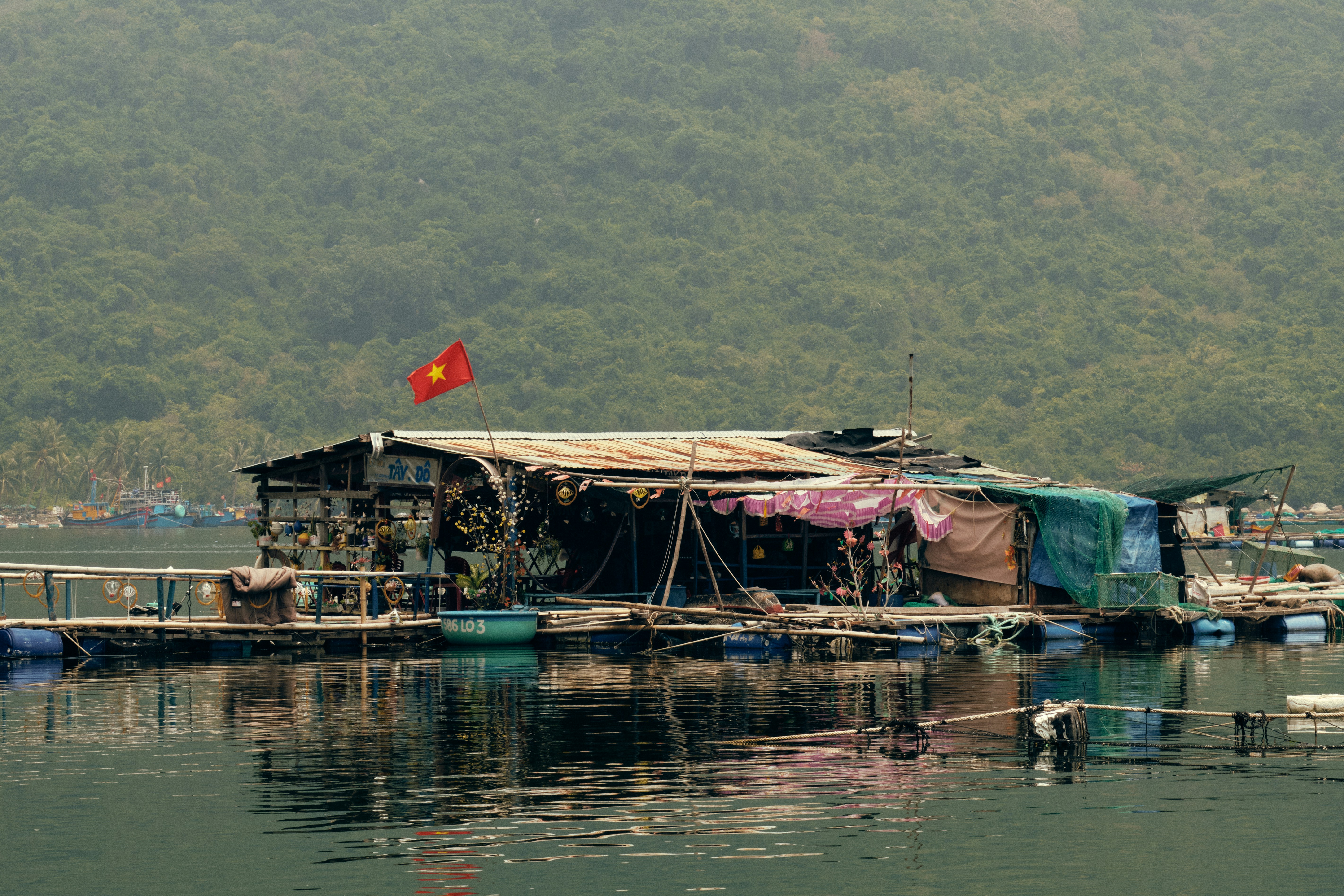 A floating house with a Vietnamese flag on water below forested hills