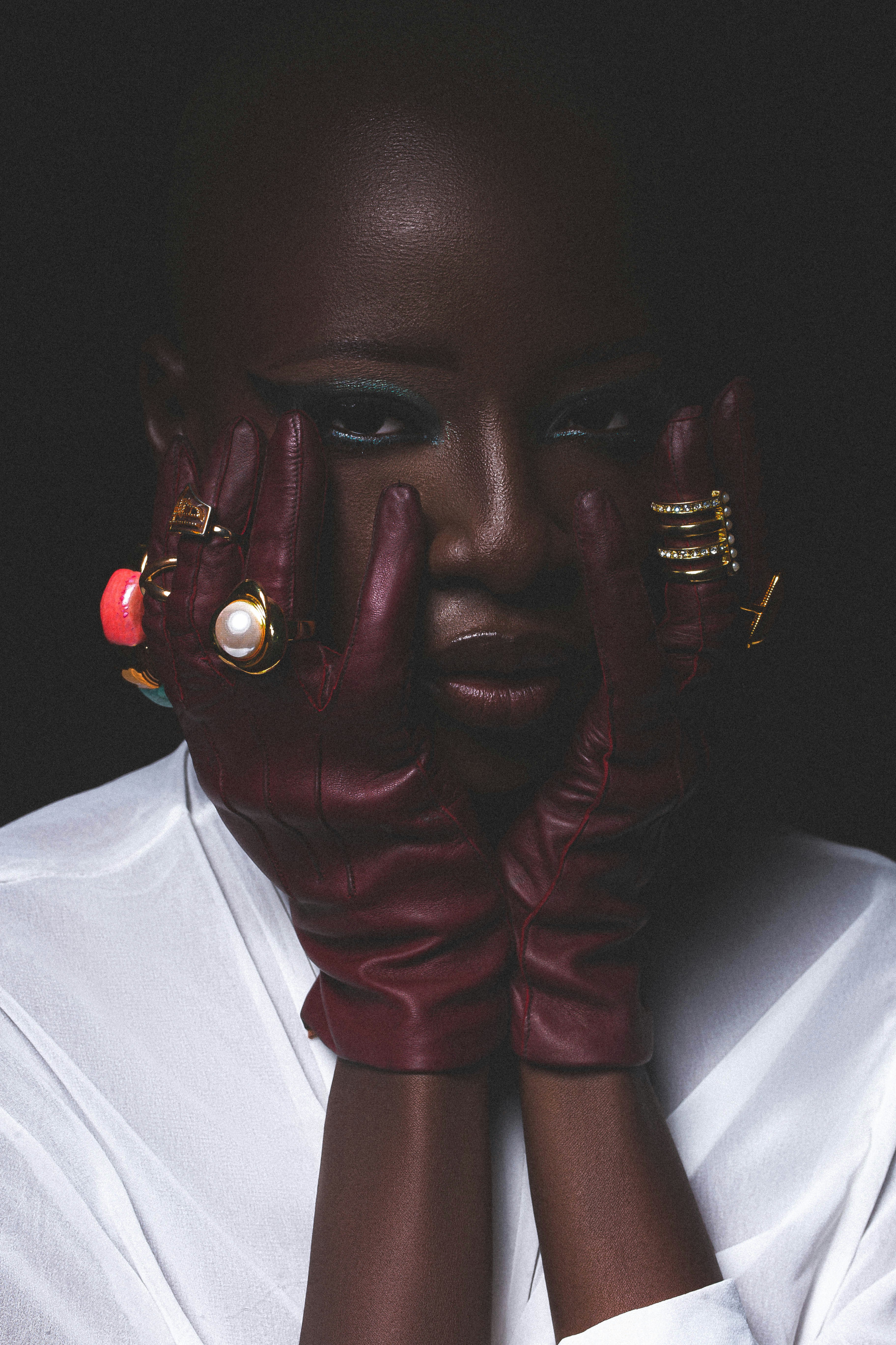 A person wearing dark red leather gloves and gold rings against a dark background