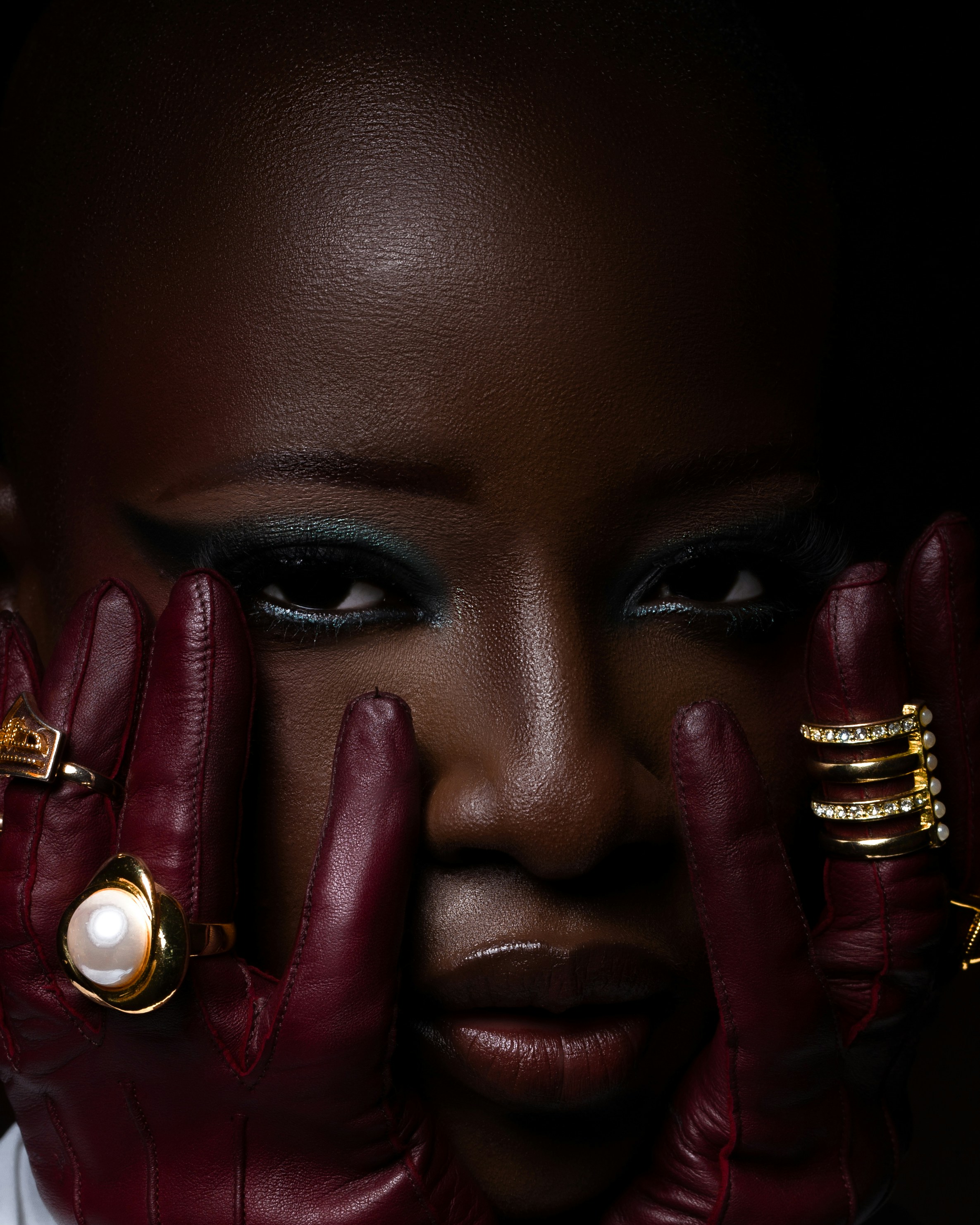 A person with dark skin wearing maroon leather gloves and gold rings