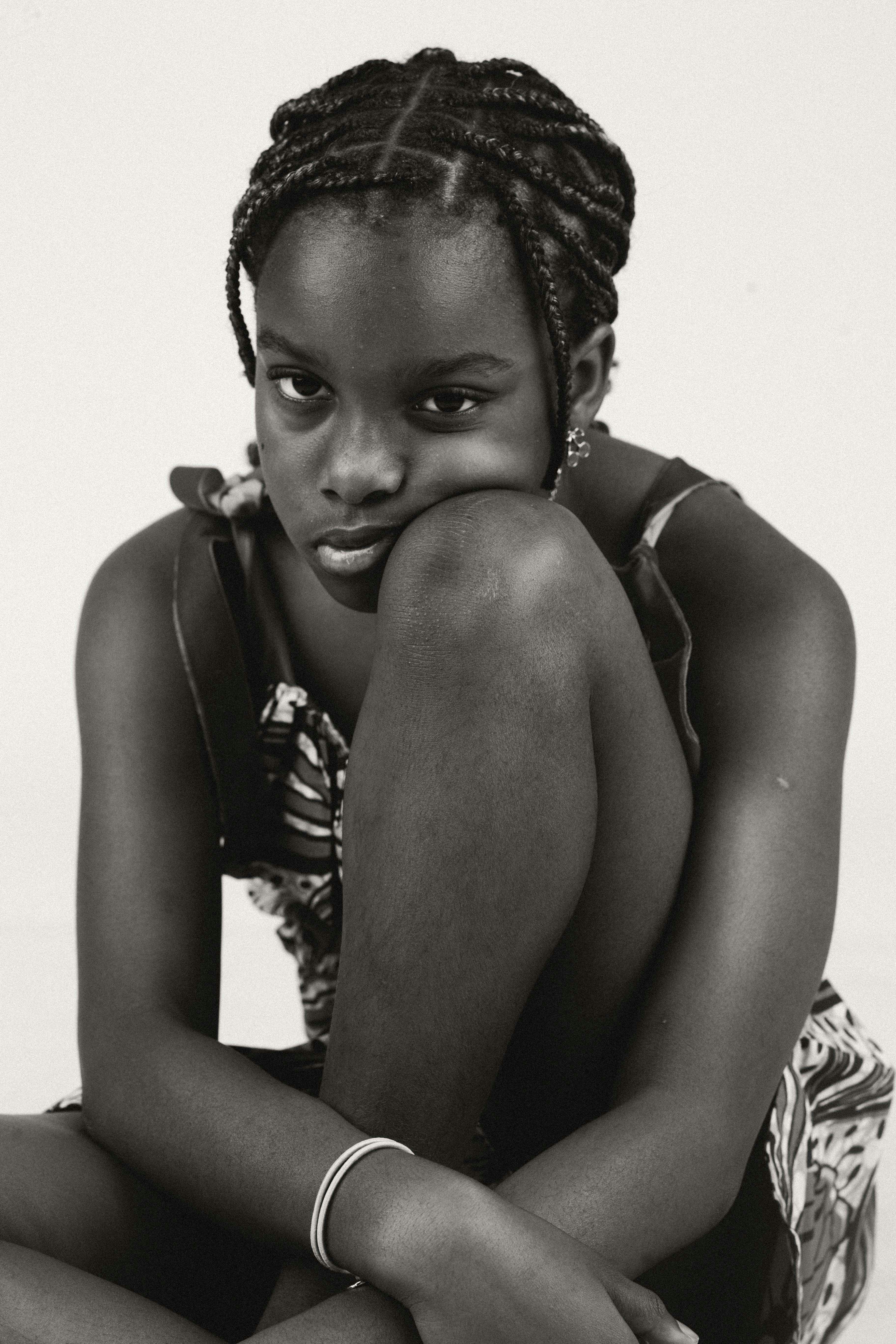 A young girl with braided hair resting her chin on her knee
