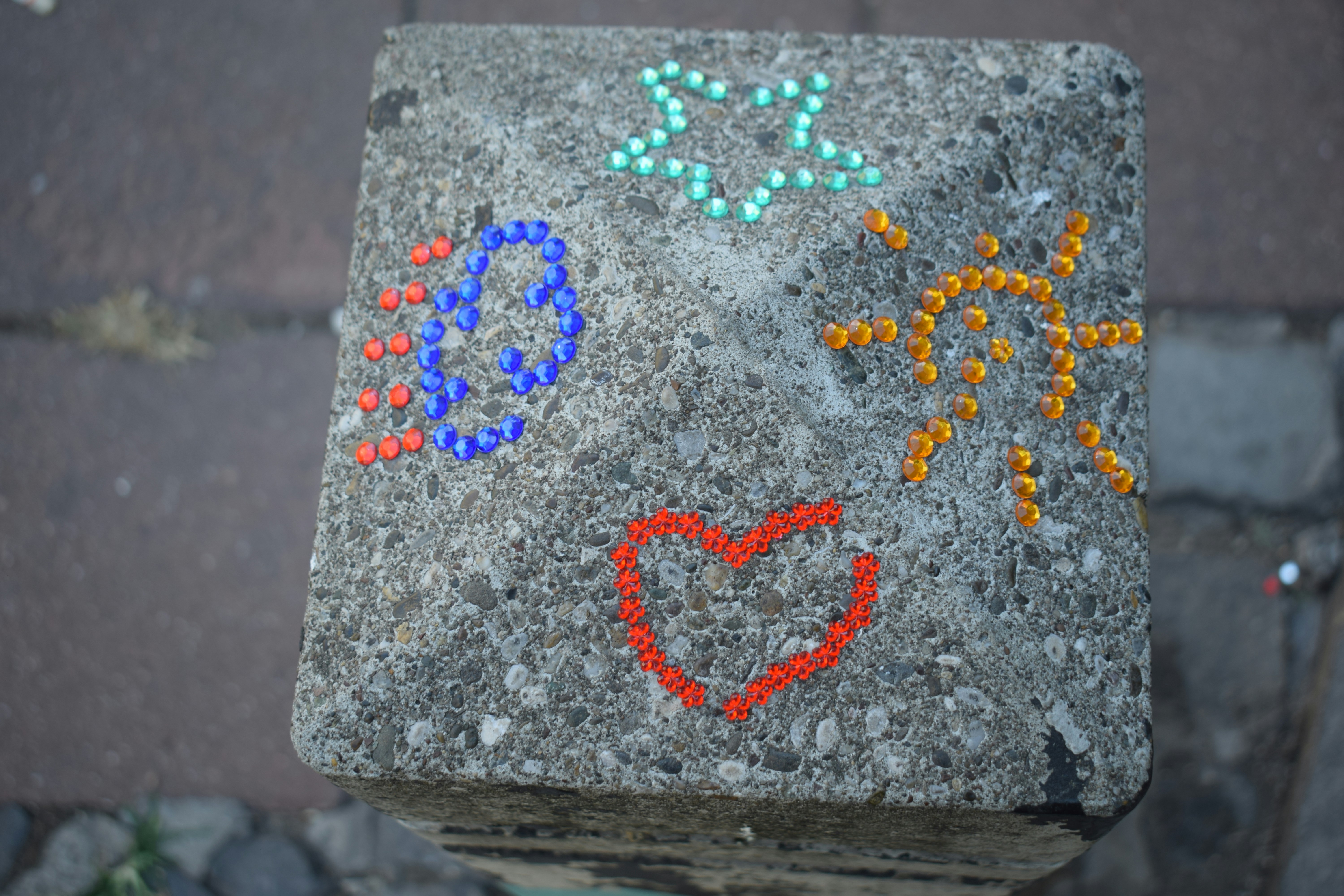 A concrete block decorated with a star, sun, heart, and cloud made of rhinestones