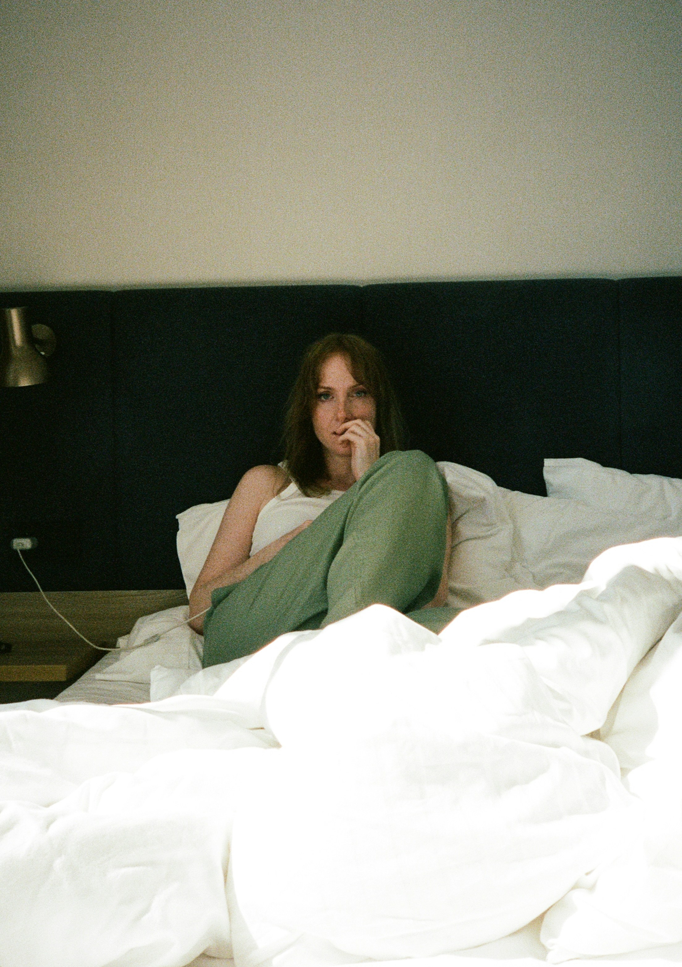 A woman in a white tank top and green pants on a bed