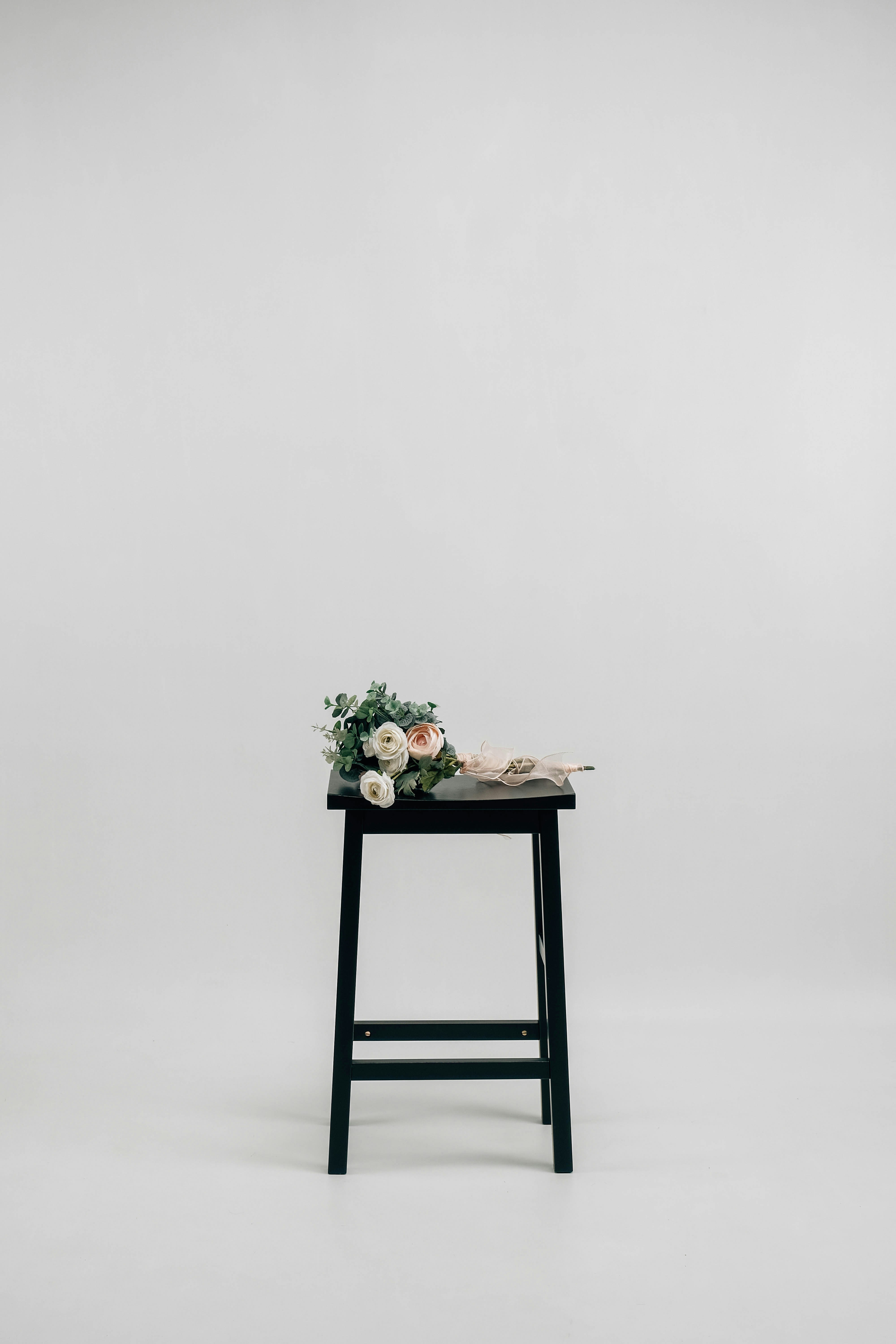 A floral bouquet with pale roses on a black wooden stool