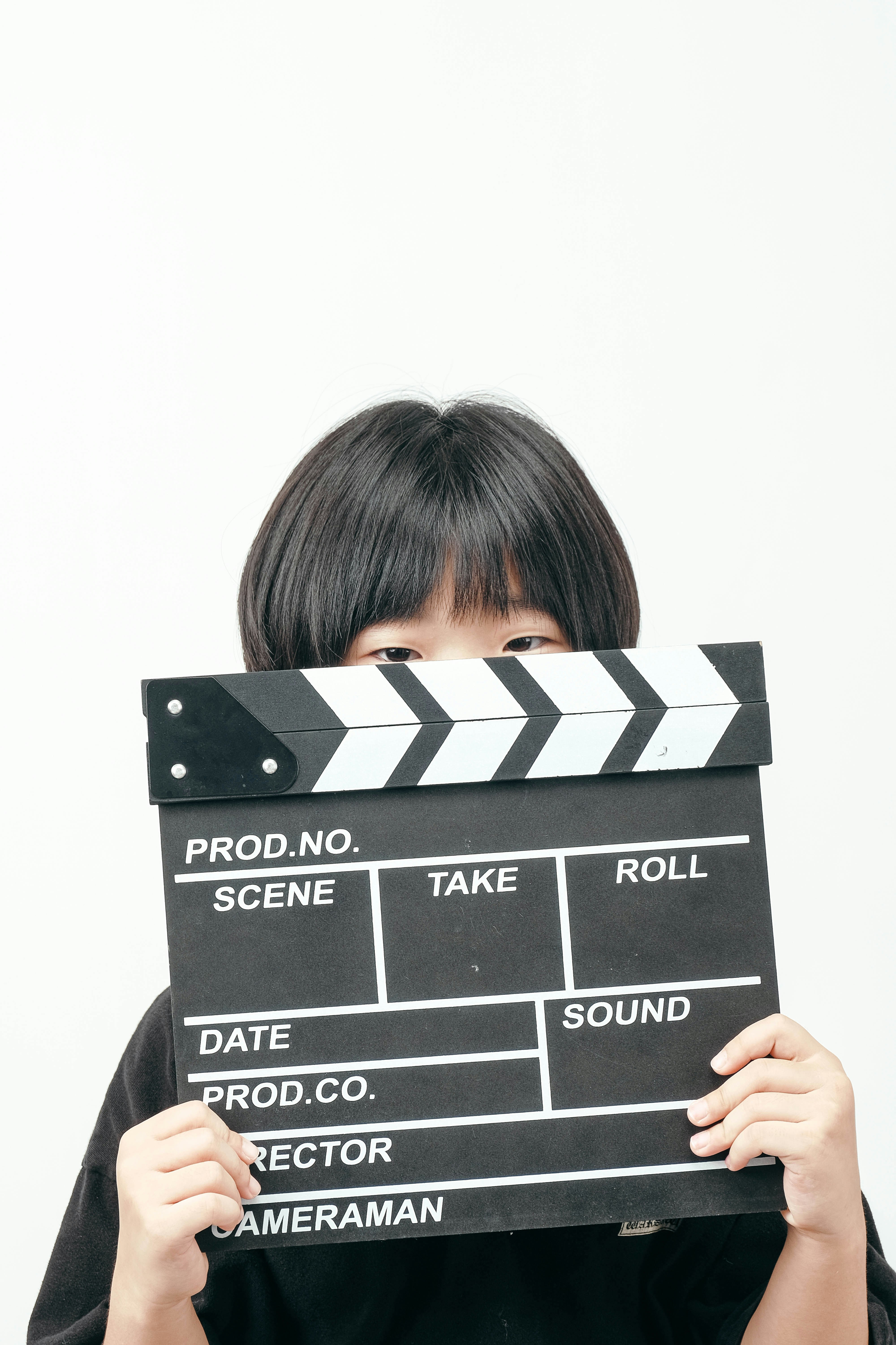 A person holding a black film clapperboard in front of their face