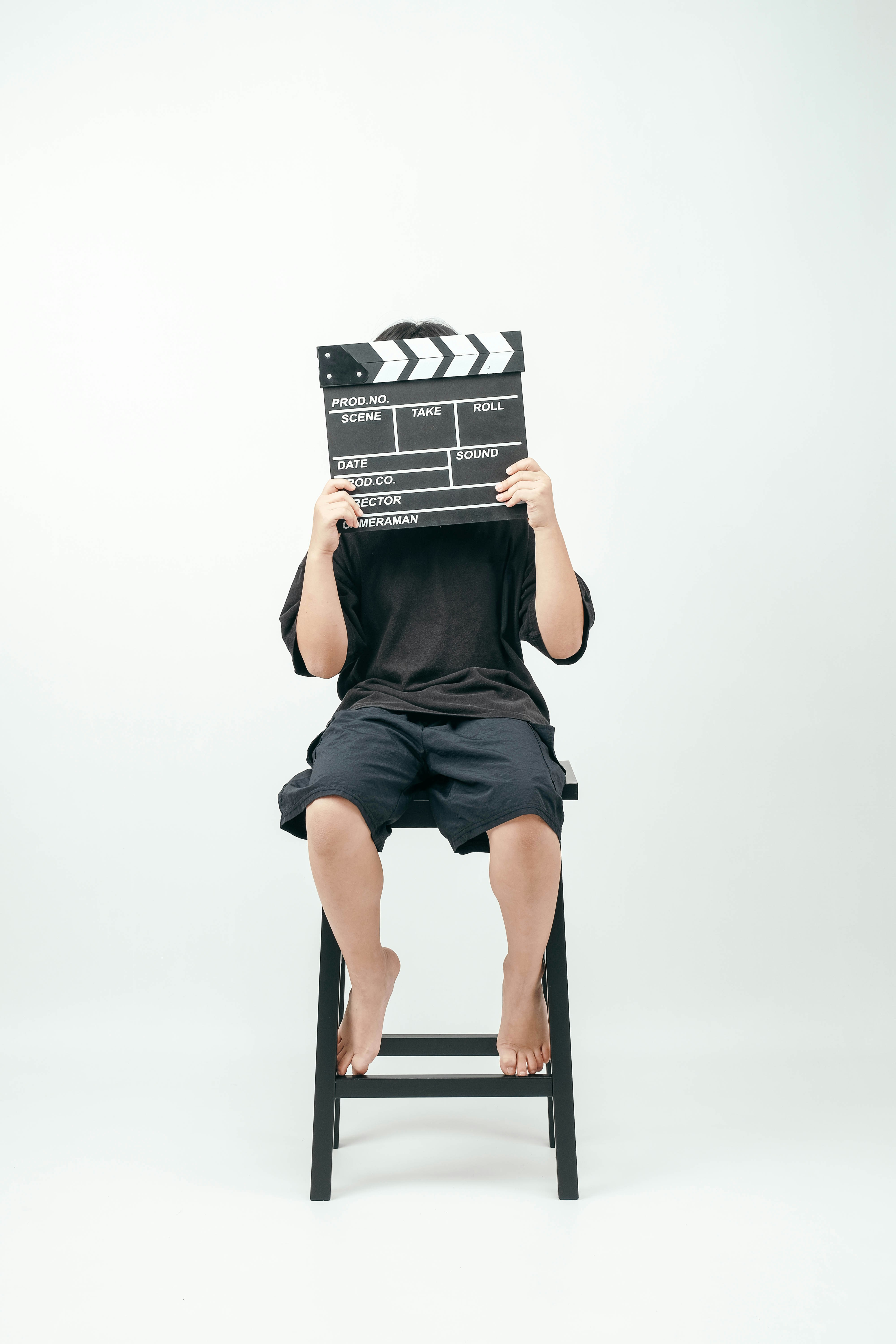 A person in a black t-shirt and shorts holding a film clapperboard