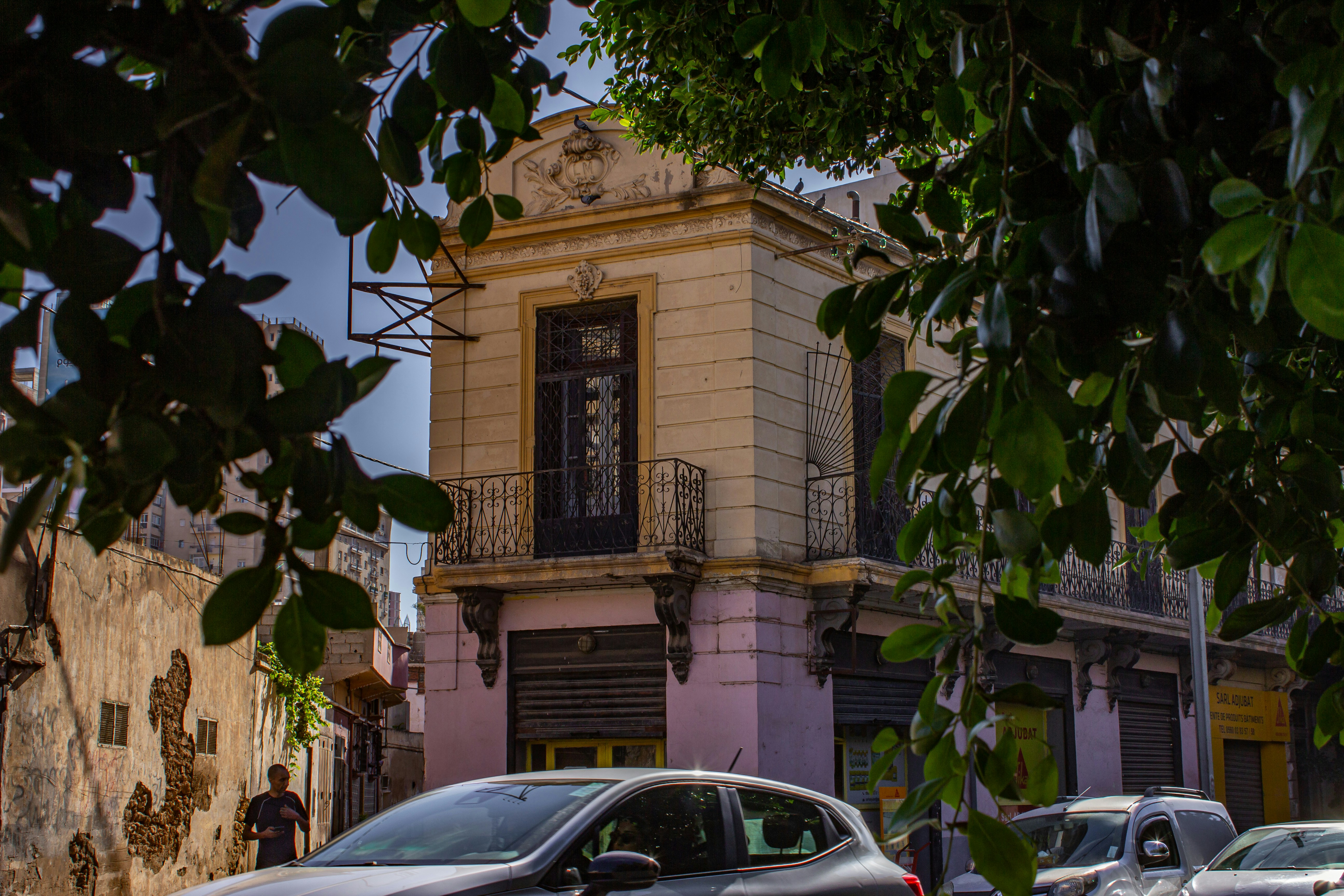 A historic building with a balcony framed by green leaves on a city street
