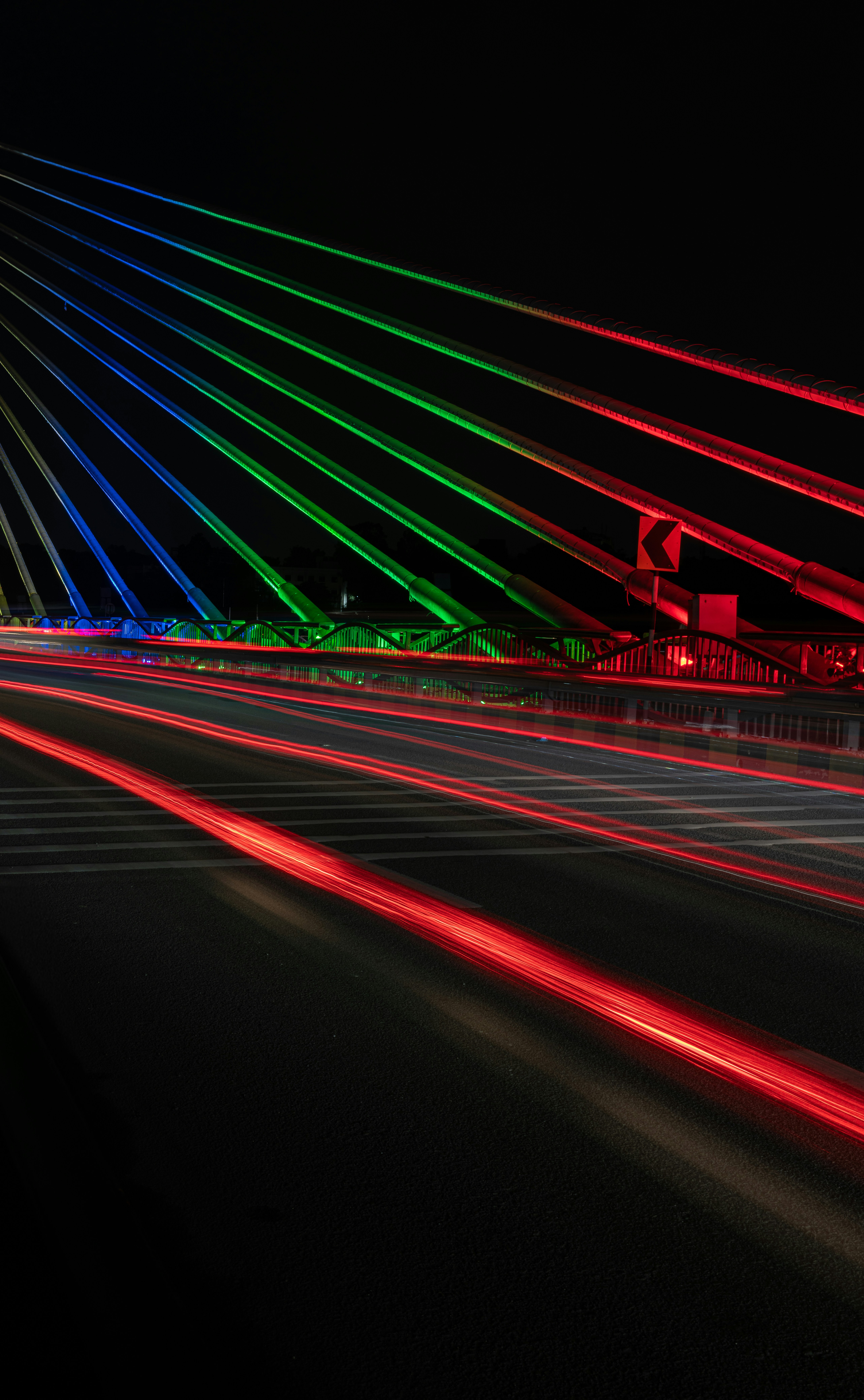 Long exposure light trails on a bridge with illuminated blue, green, and red cables