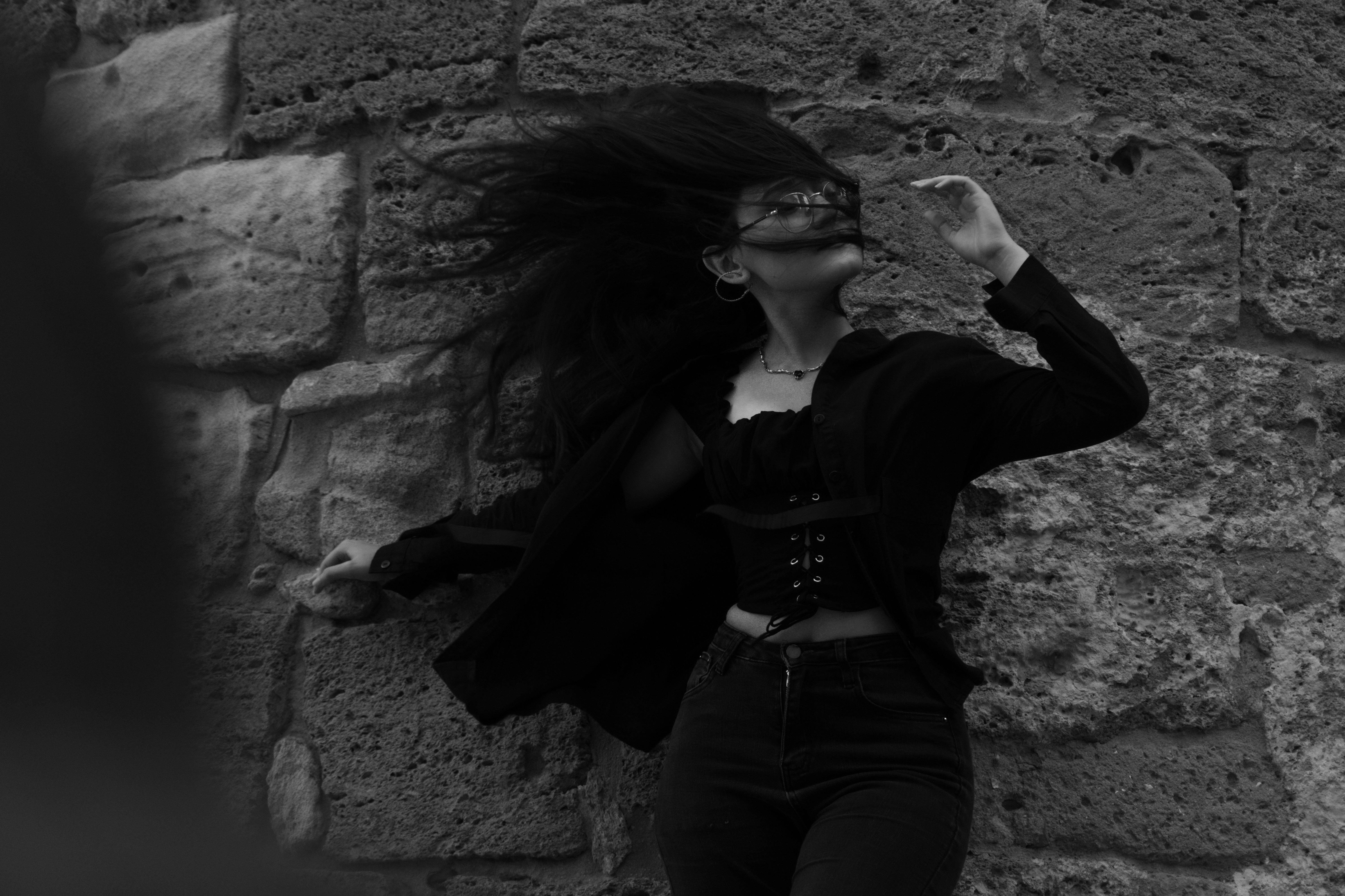 A woman with windblown hair in a black corset top against a stone wall