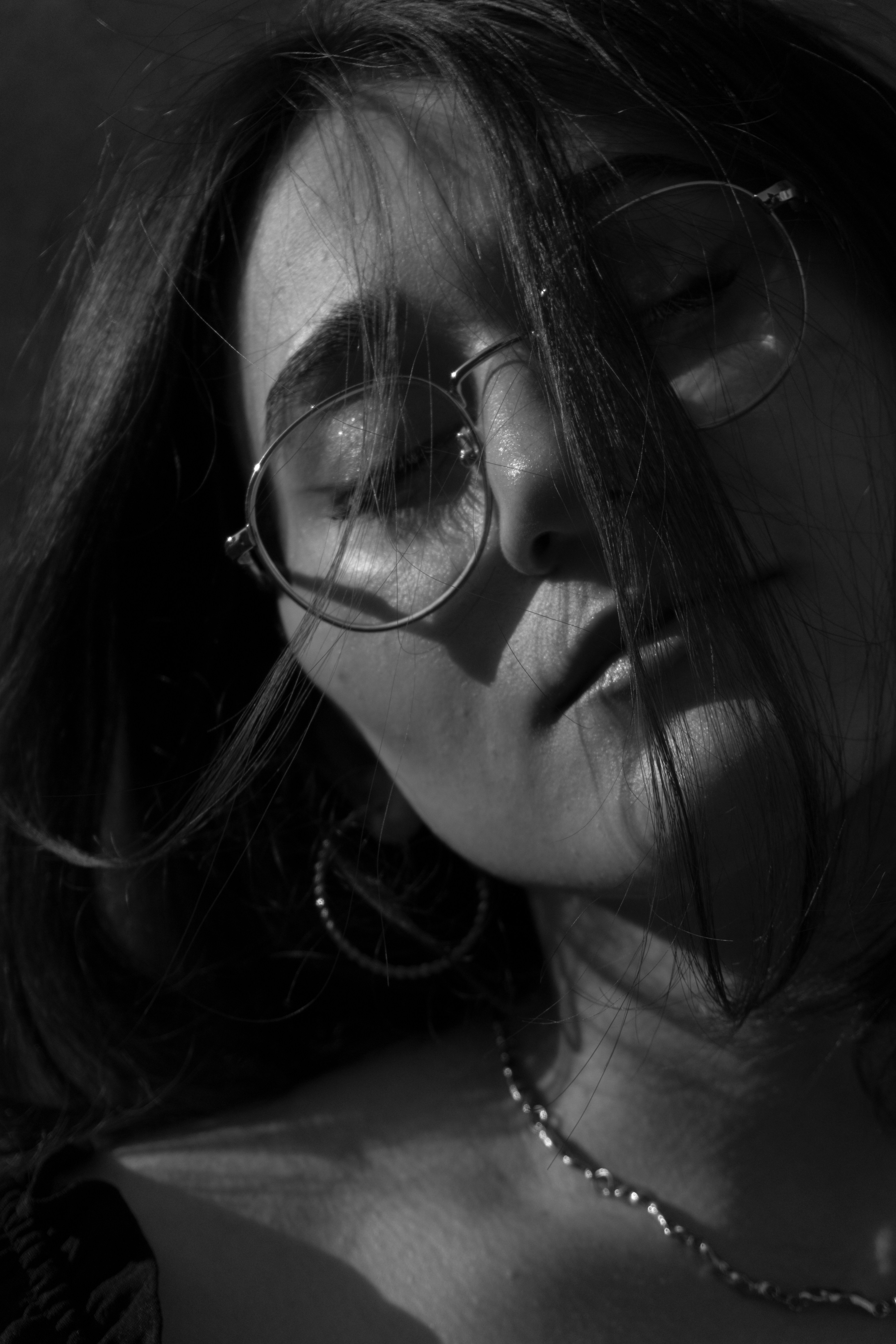 A woman with closed eyes wearing round glasses and a chain necklace