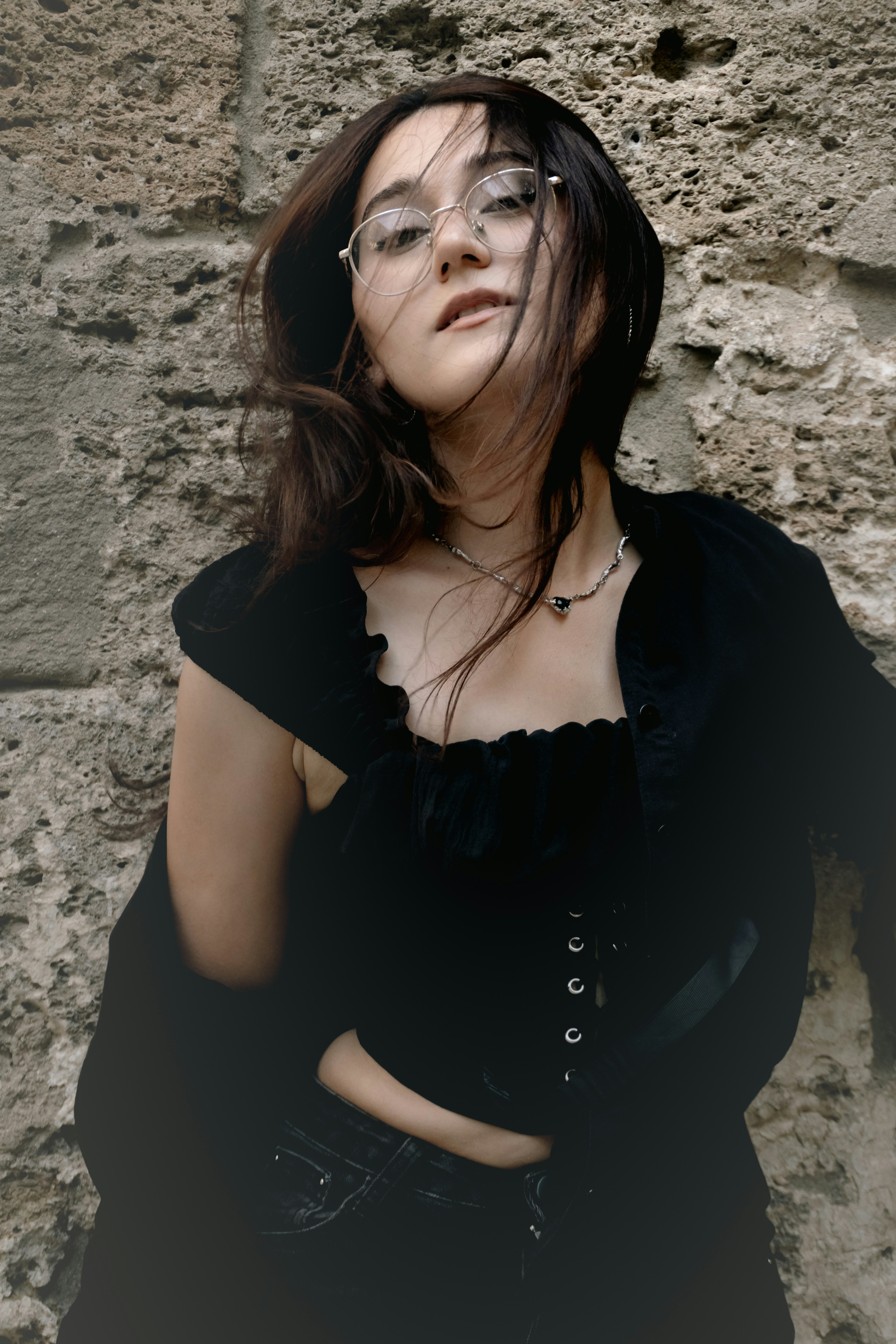 A woman with glasses and dark hair against a textured stone wall
