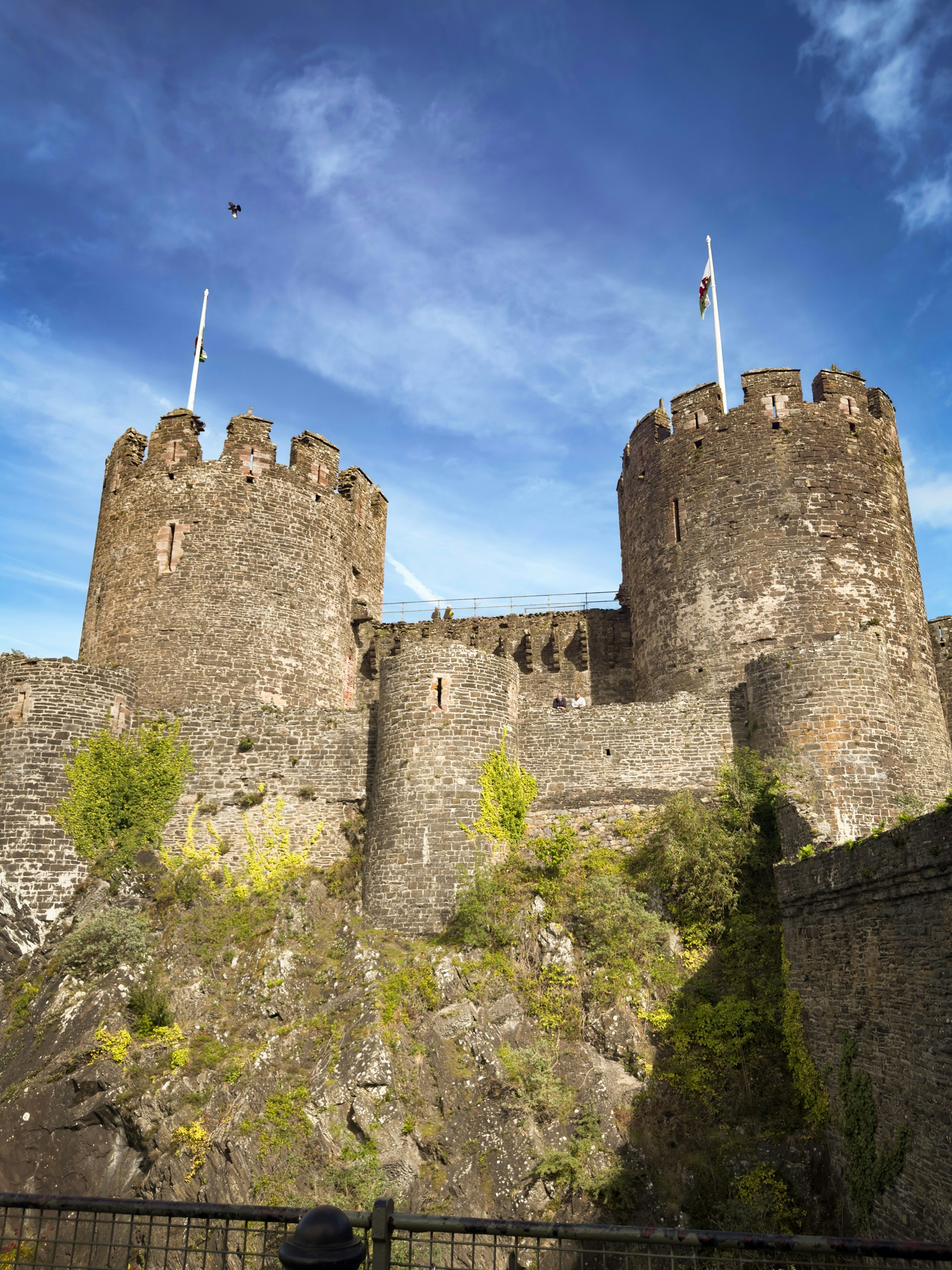 Stone towers of Conwy Castle rising above a rocky cliff under a blue sky
