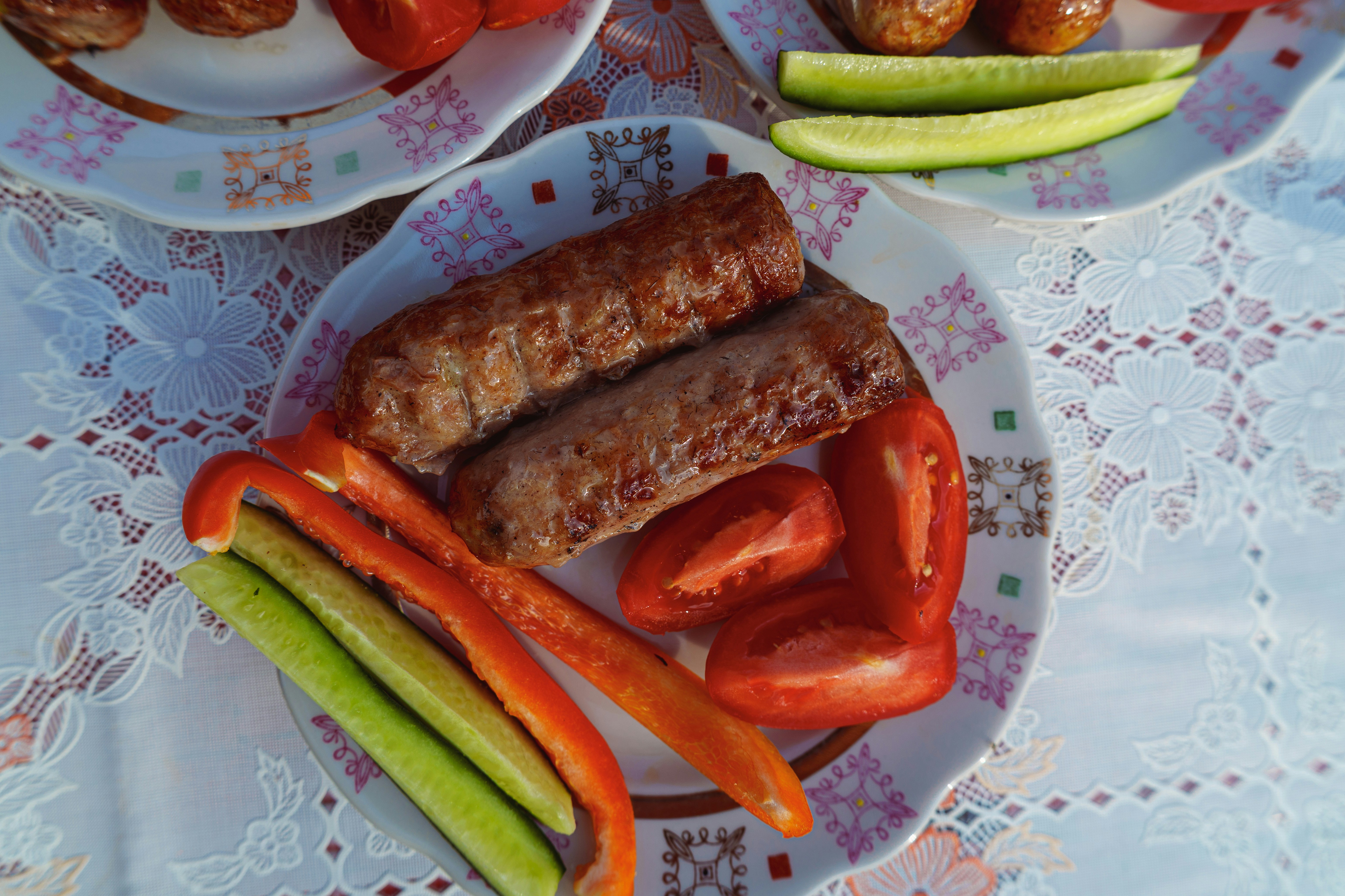 Zwei gegrillte Würstchen mit geschnittenen roten Paprika, Tomaten und Gurken auf einem Teller