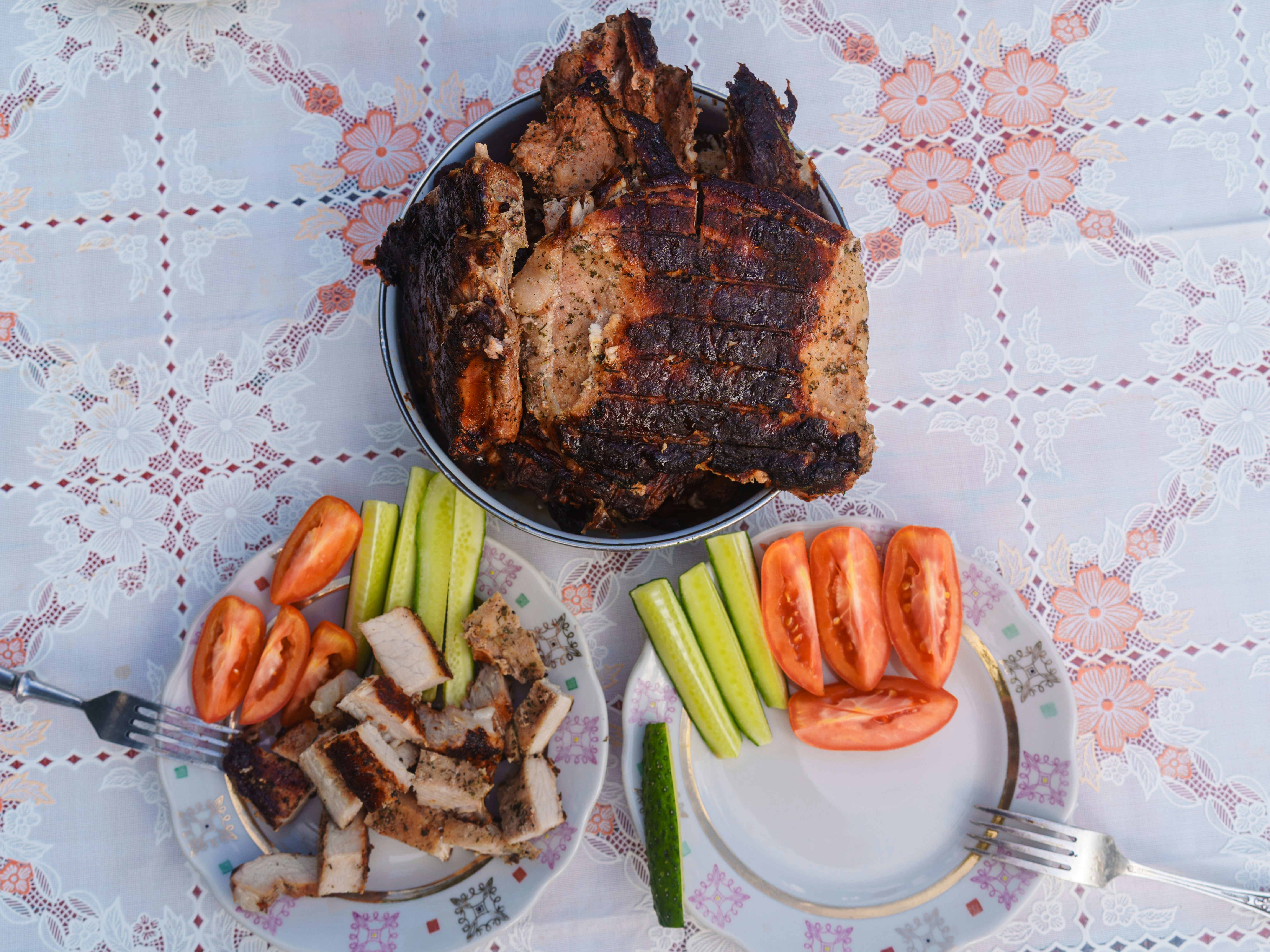 Gegrilltes Schweinefleisch, geschnittene Gurken und Tomatenscheibe auf Tellern auf einer floralen Tischdecke