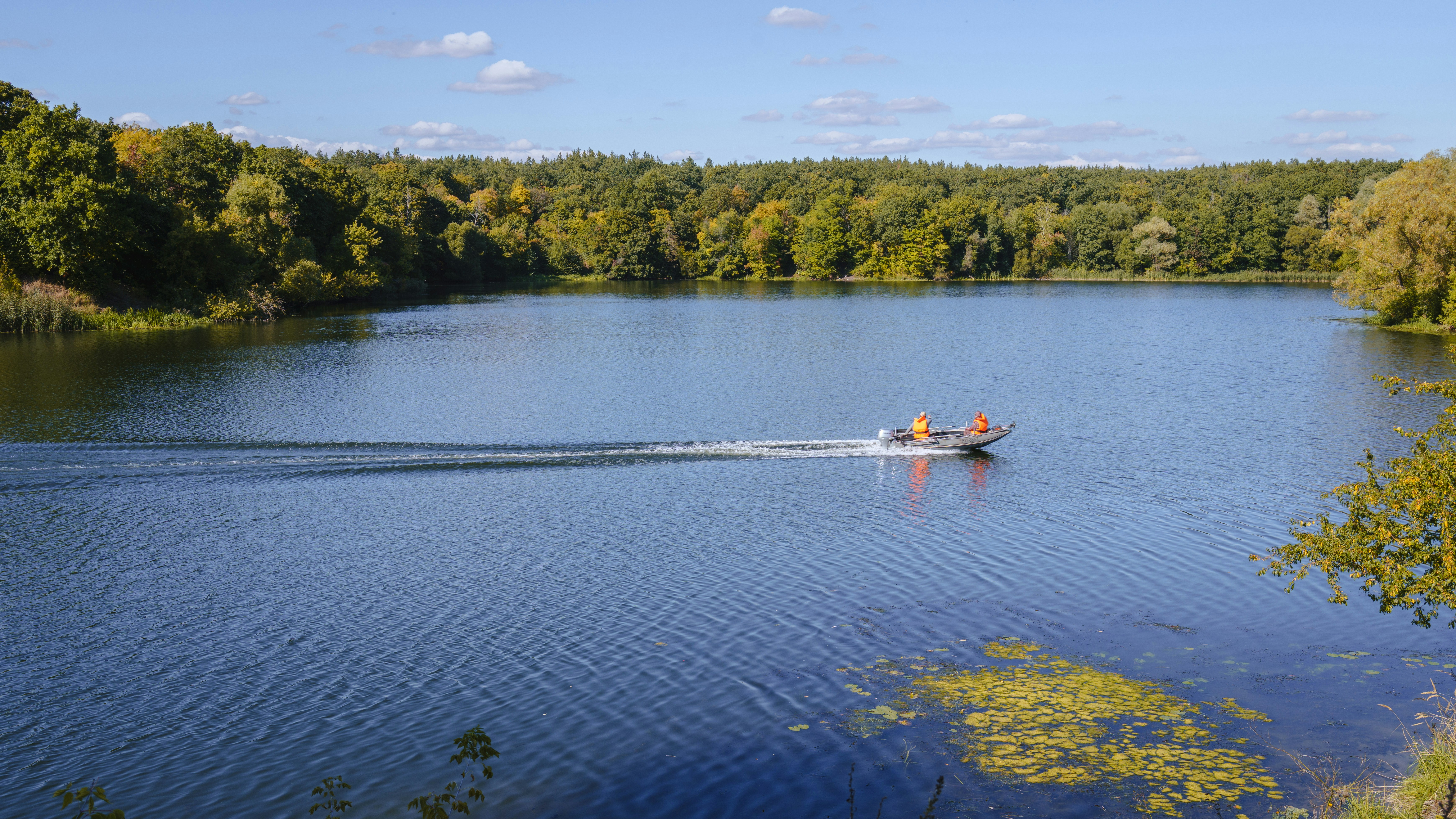 Ein Motorboot mit zwei Personen in orangefarbenen Schwimmwesten, die einen ruhigen See überqueren