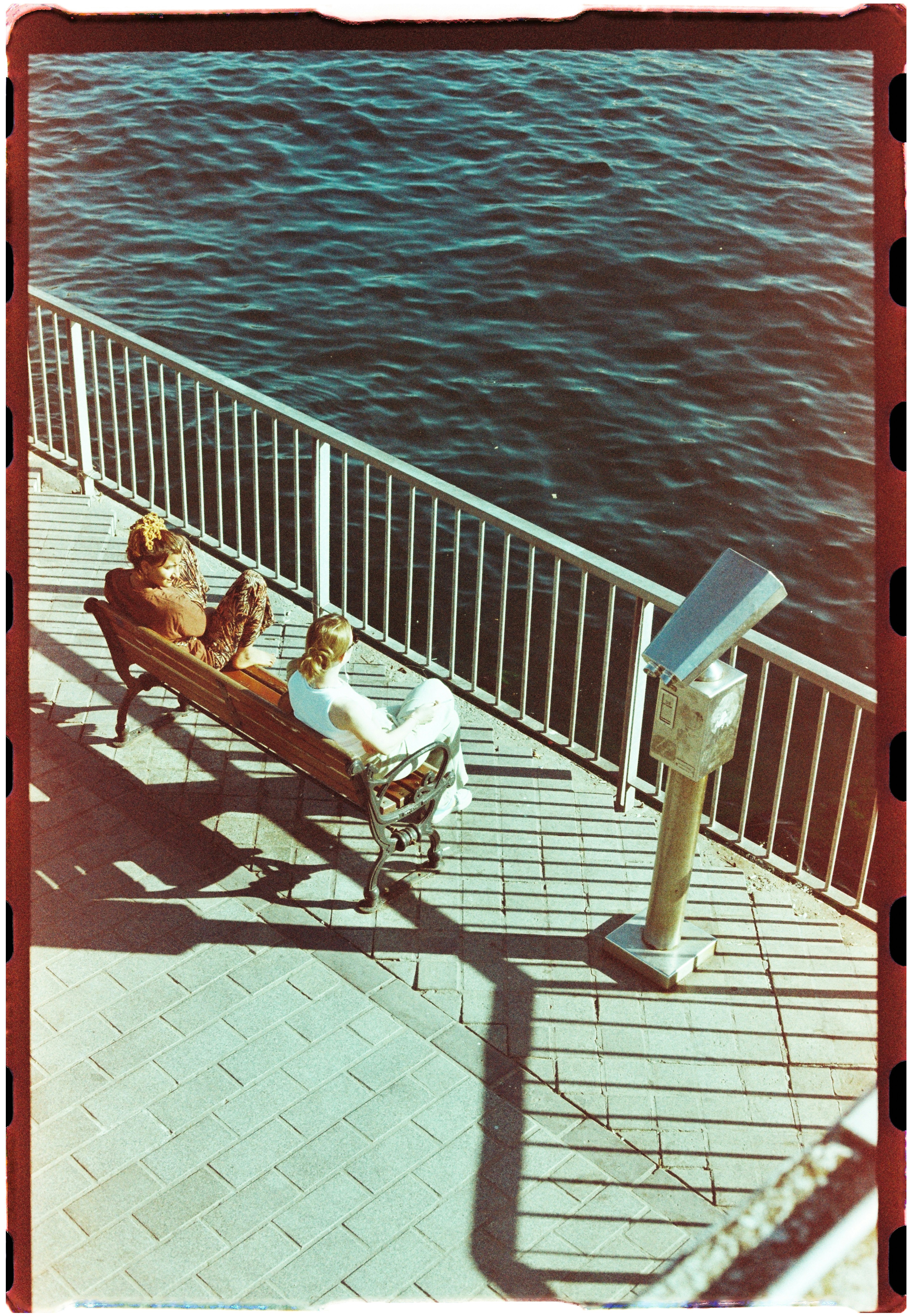 Two people on a bench beside a metal railing overlooking dark water