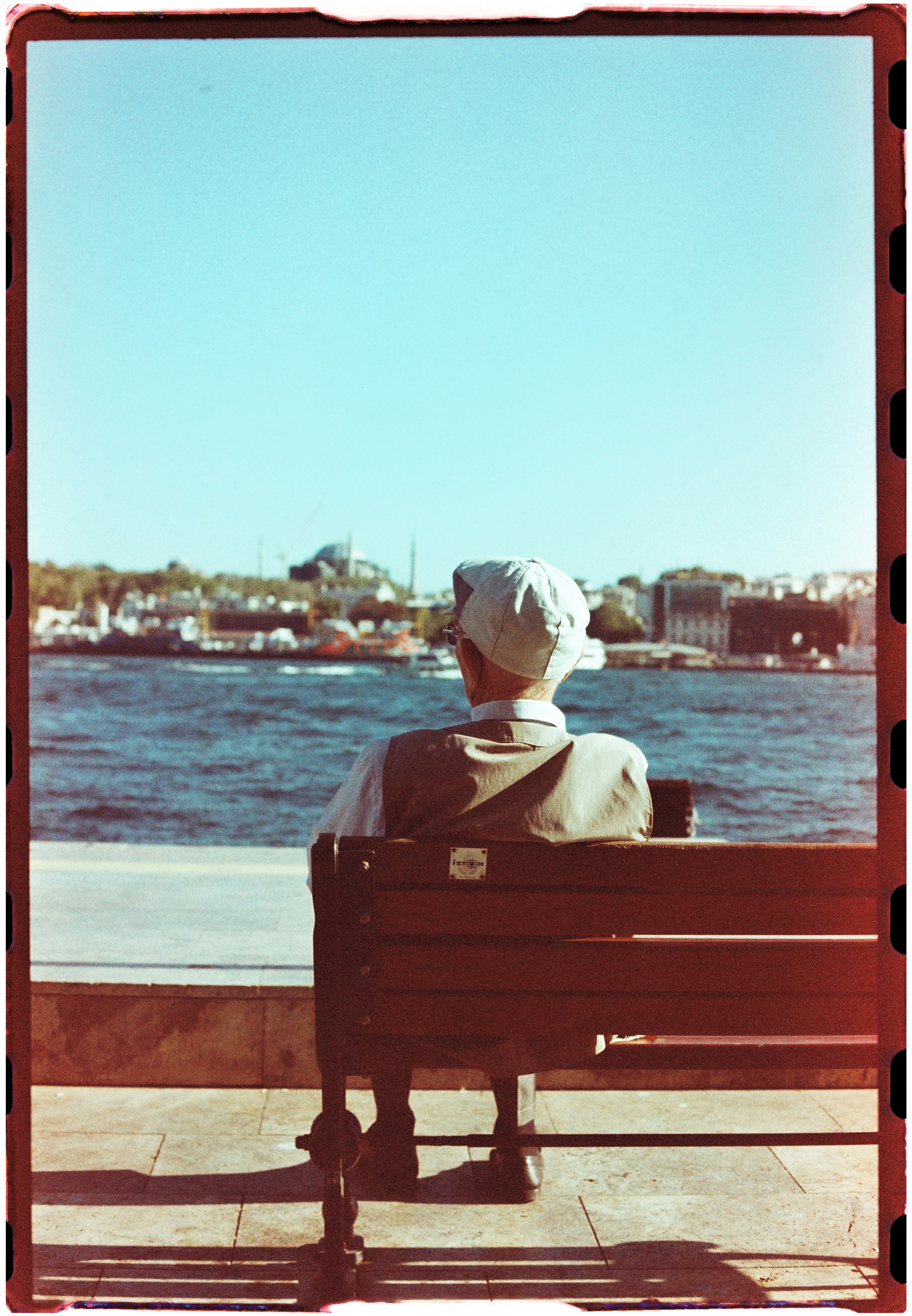 A person in a flat cap on a wooden bench overlooking a body of water