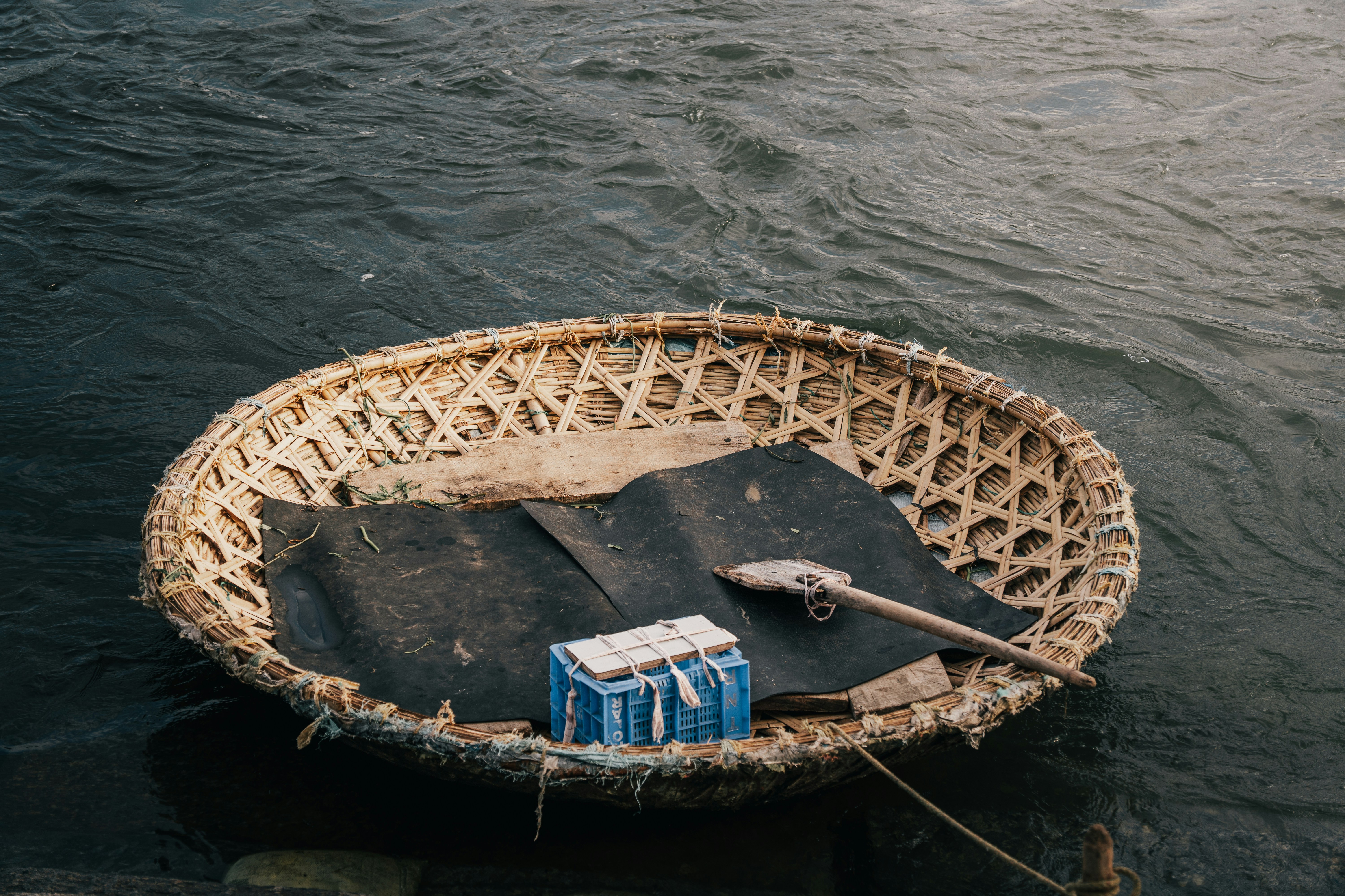 A round woven coracle boat with a wooden paddle on dark river water