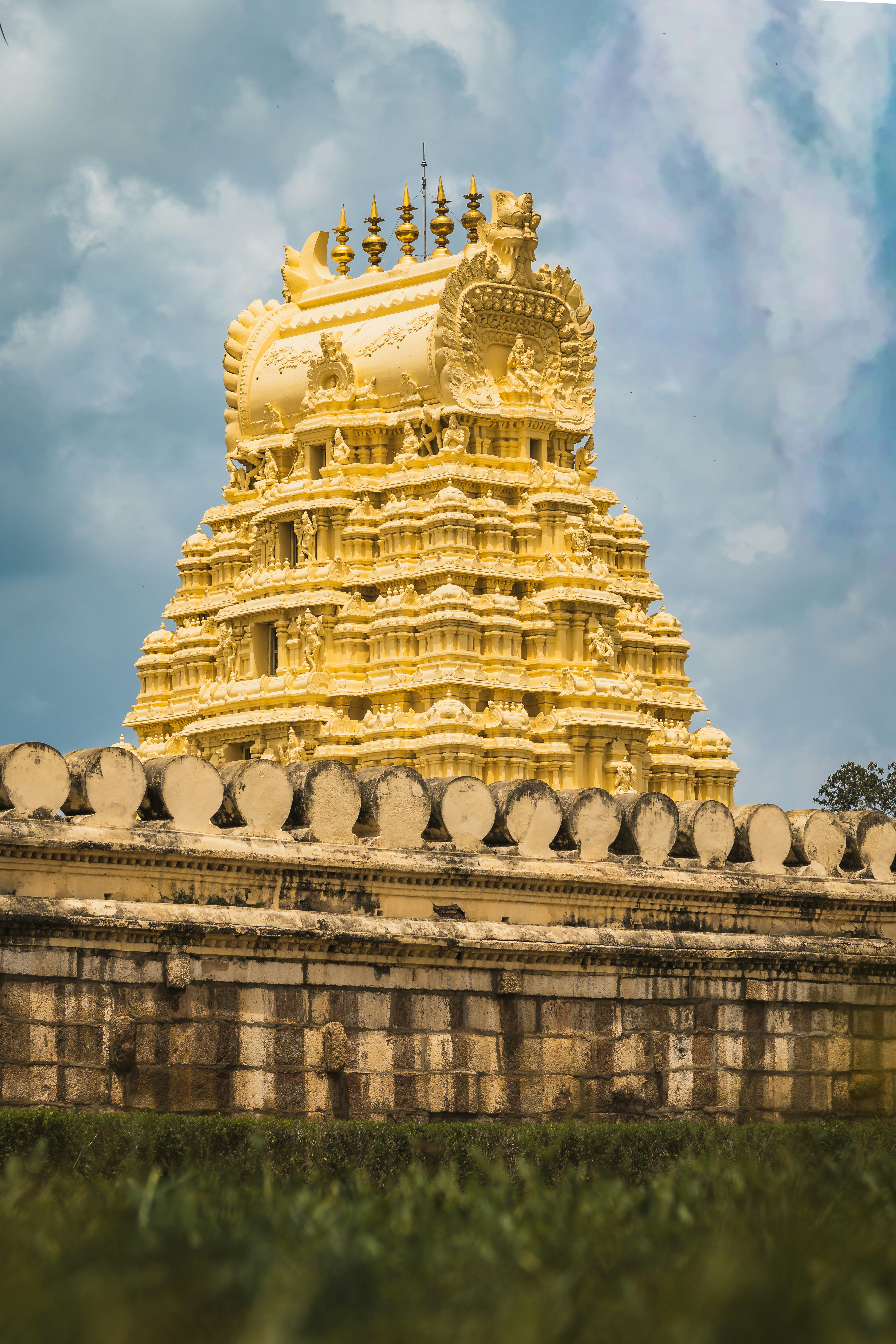 A yellow ornate temple tower rising above a stone wall against a cloudy sky