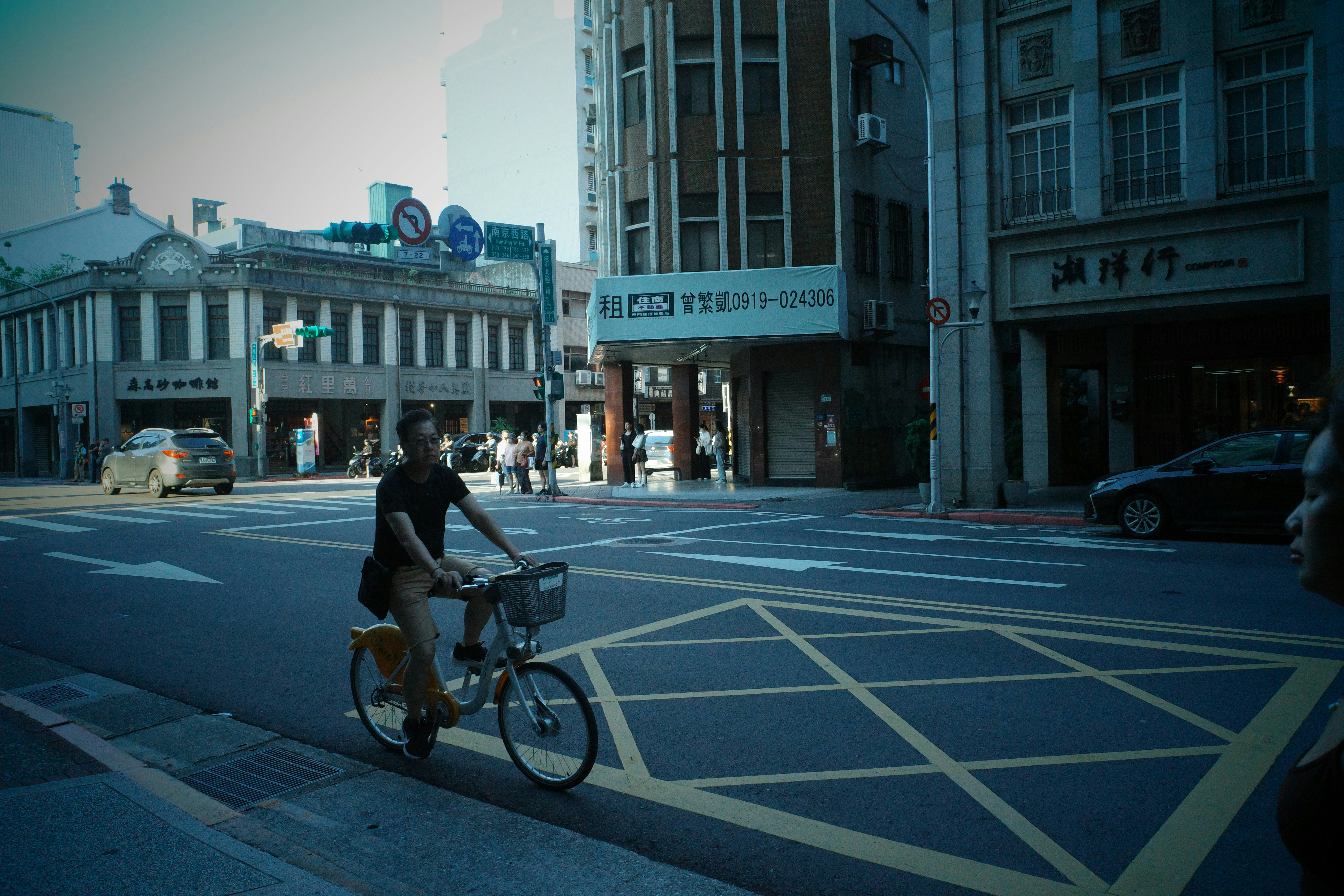 A person cycling a bike with a basket across a city intersection
