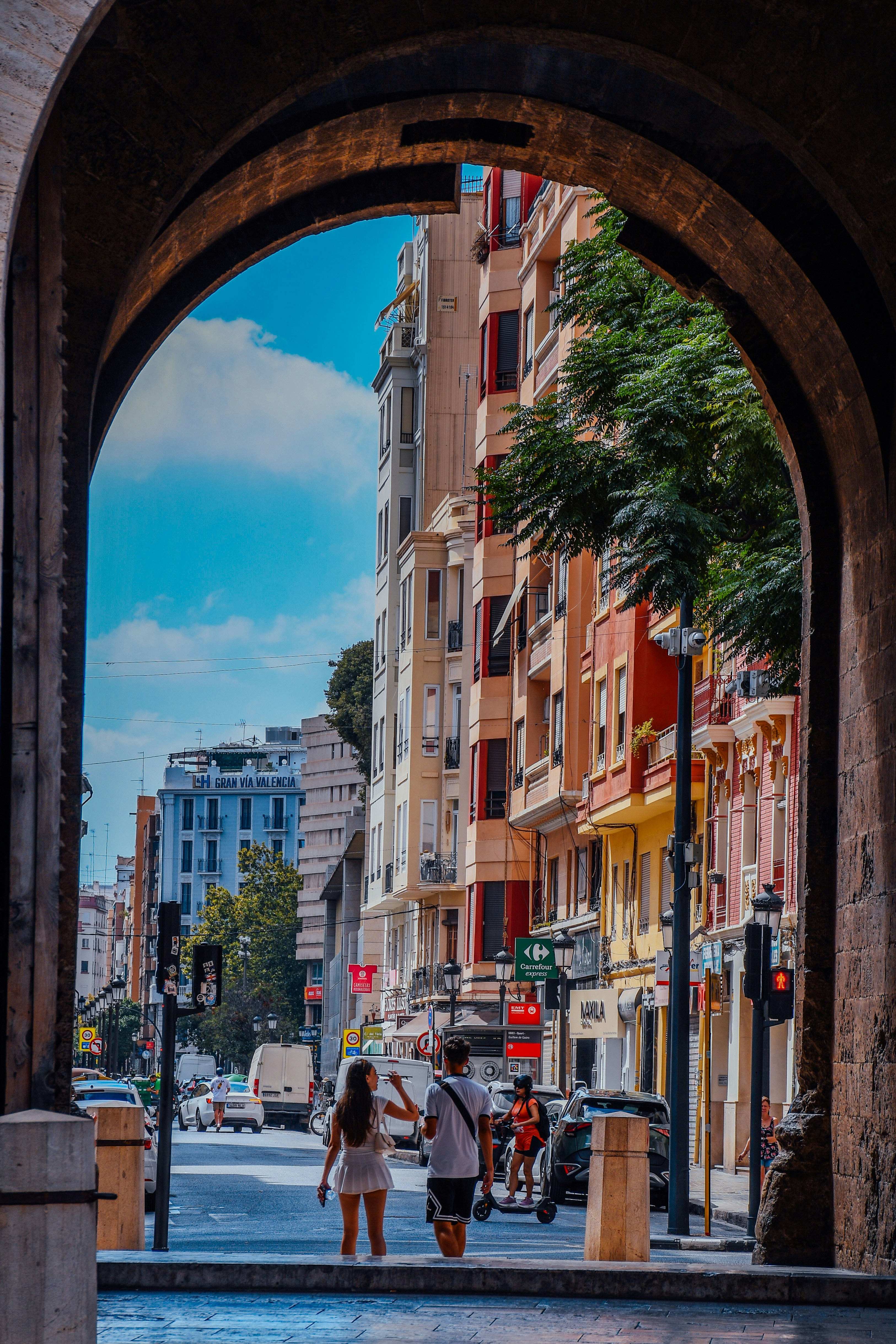 People walking on a street in Valencia framed by a stone archway