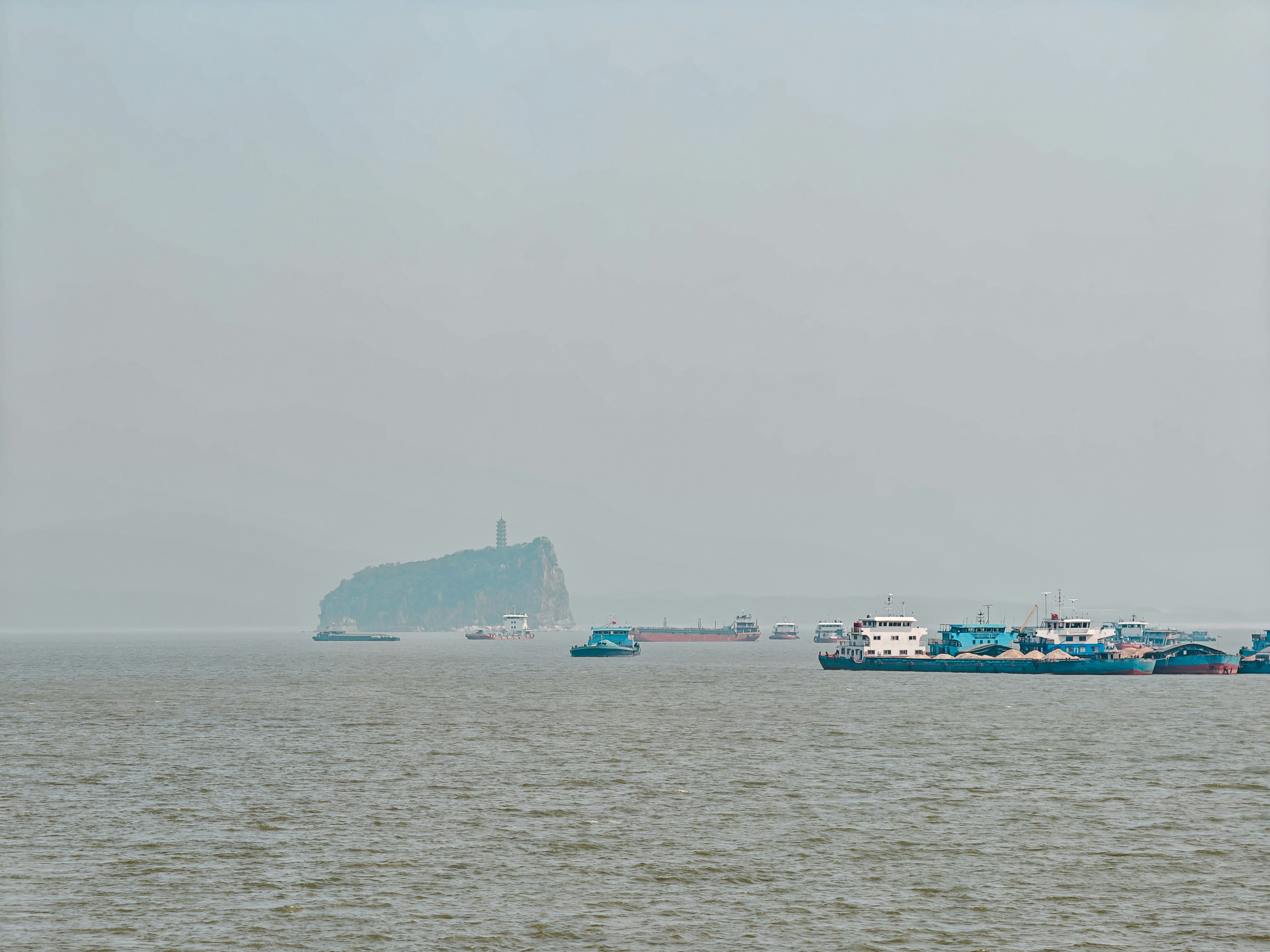 Cargo ships on a hazy river with a pagoda on a distant island