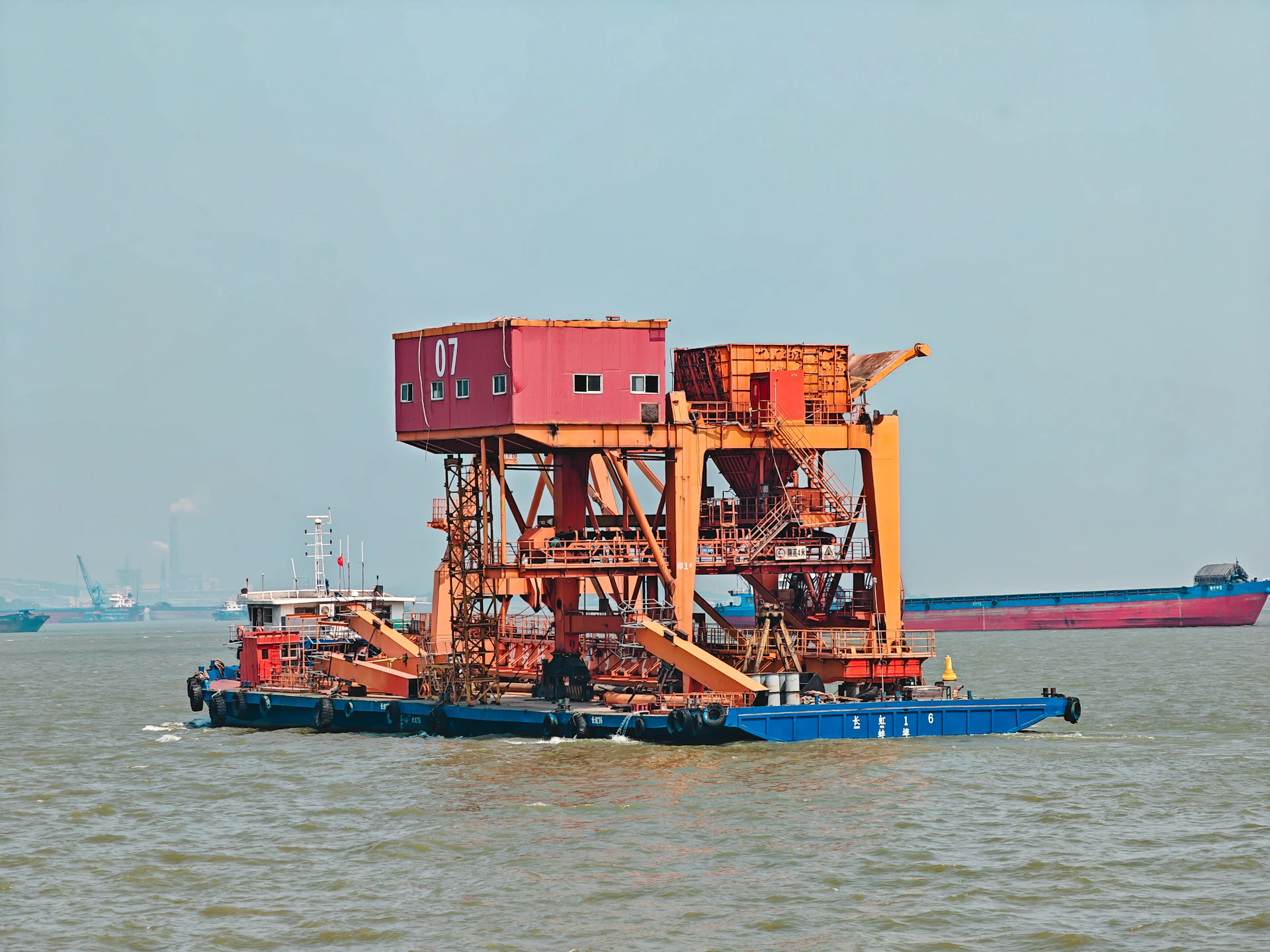 A large orange industrial crane barge on calm water with a blue hull