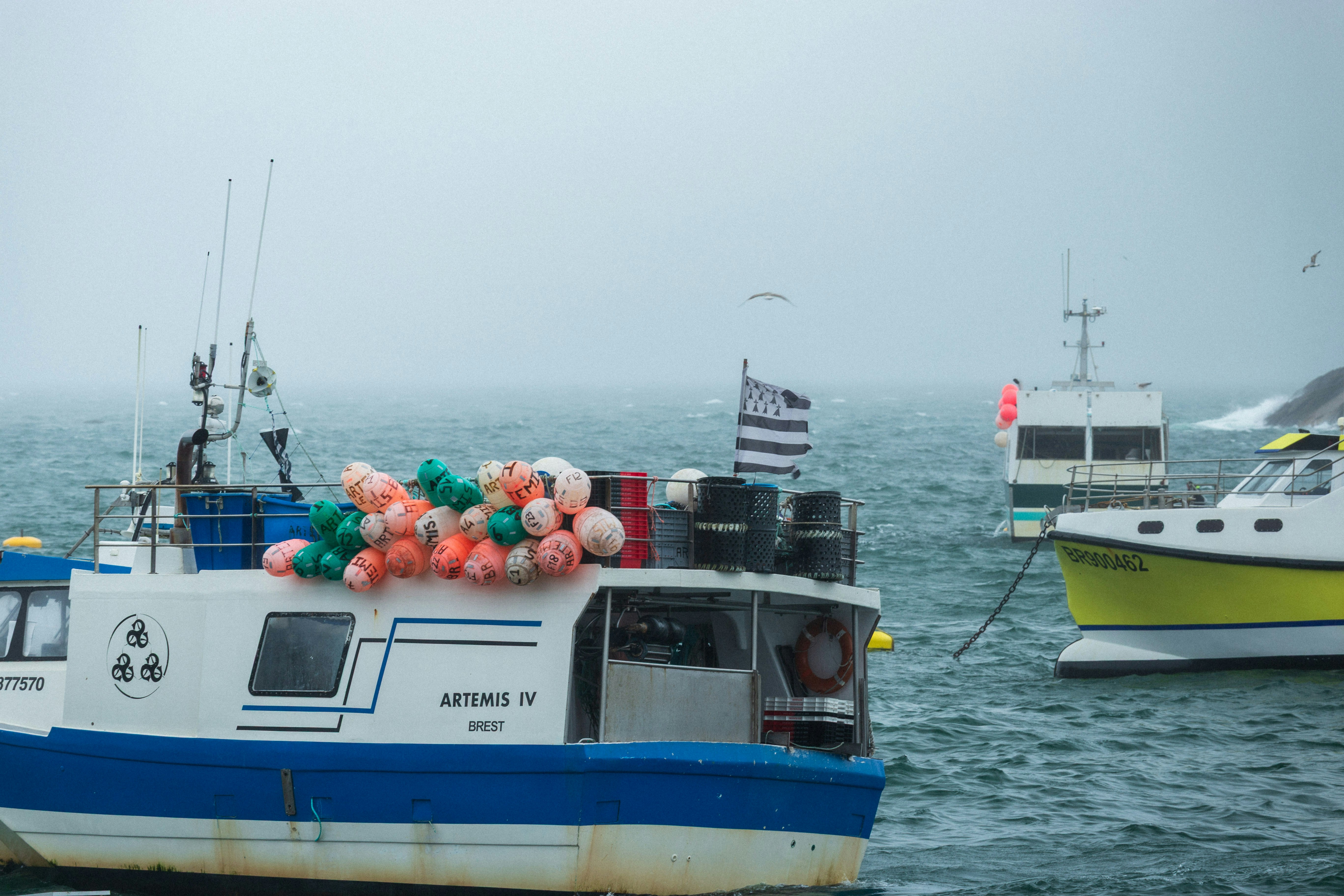 Fishing boats with colorful buoys and a Breton flag on choppy water in Brest