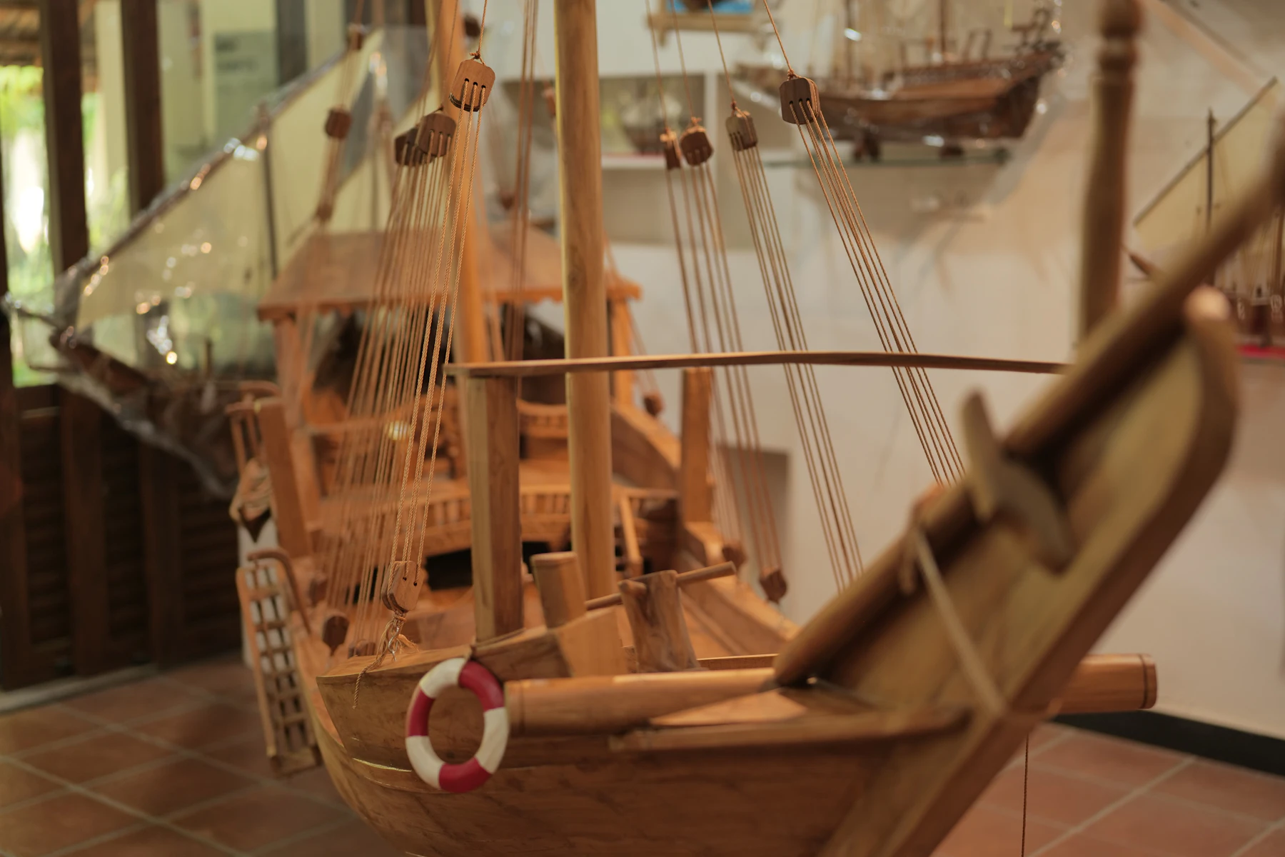 An unpainted wooden model ship with rope rigging and a red and white lifebuoy on its side