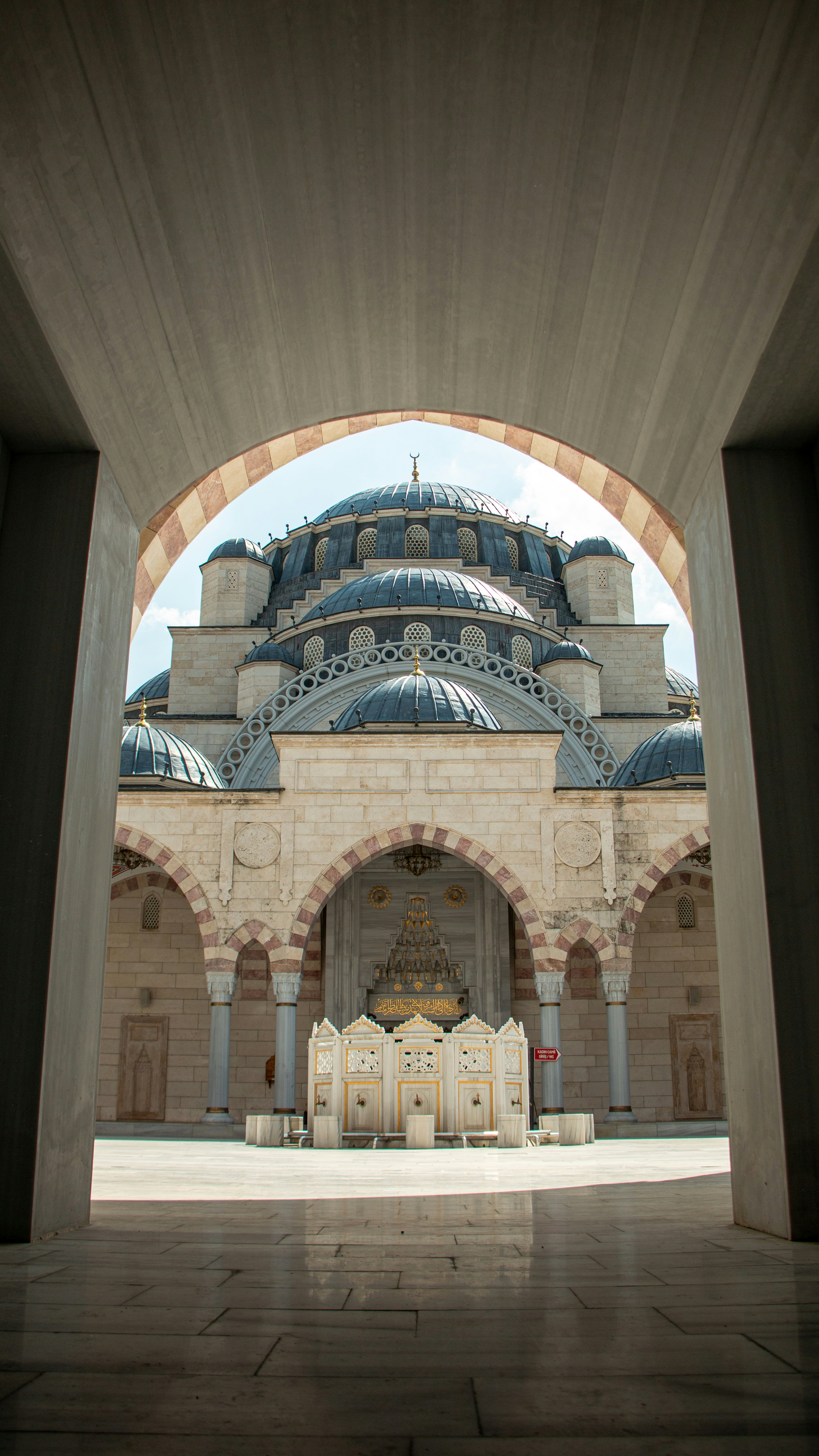 A stone ablution fountain in the courtyard of a large mosque with domed roofs