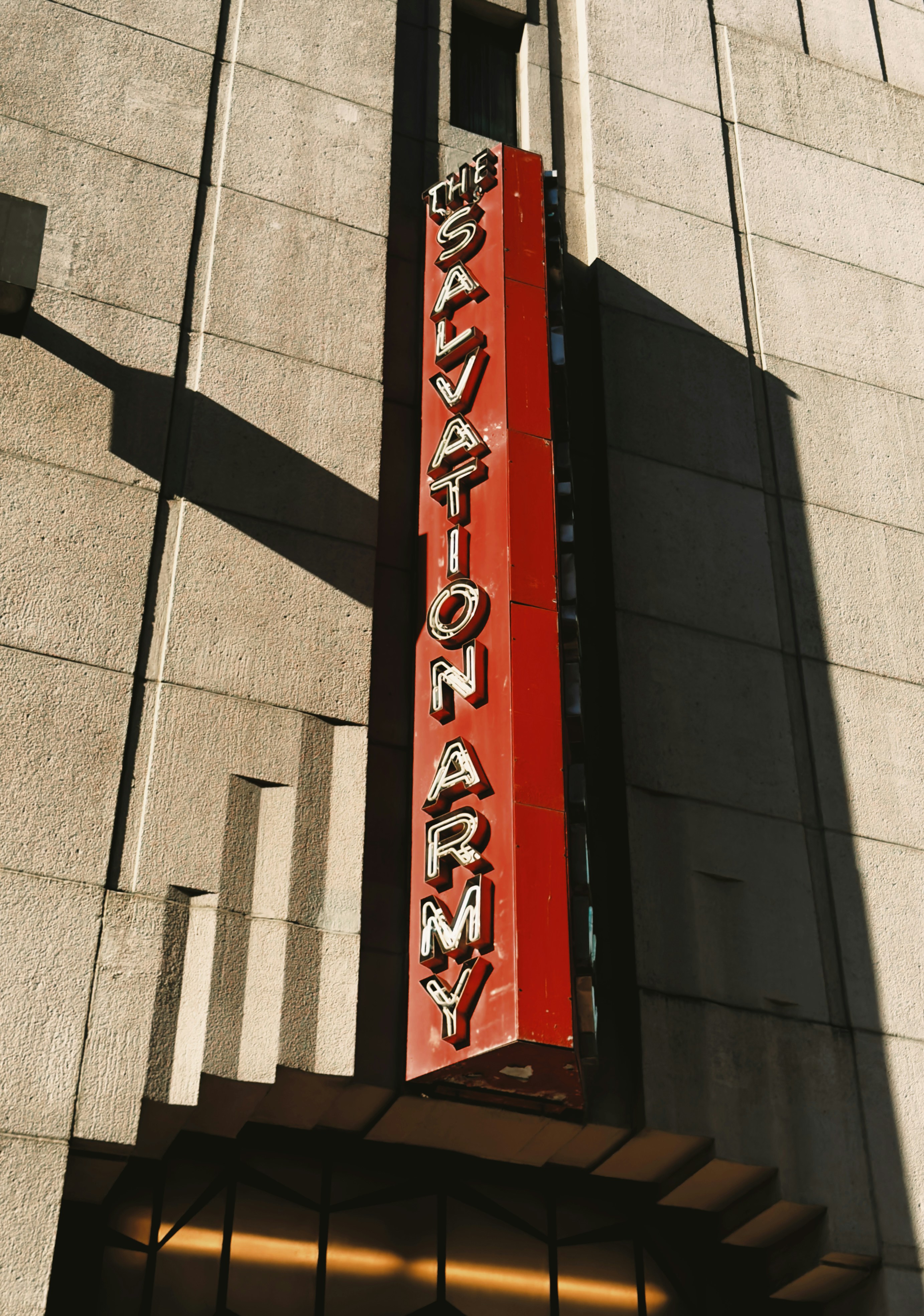 A vertical red Salvation Army sign on a stone building facade