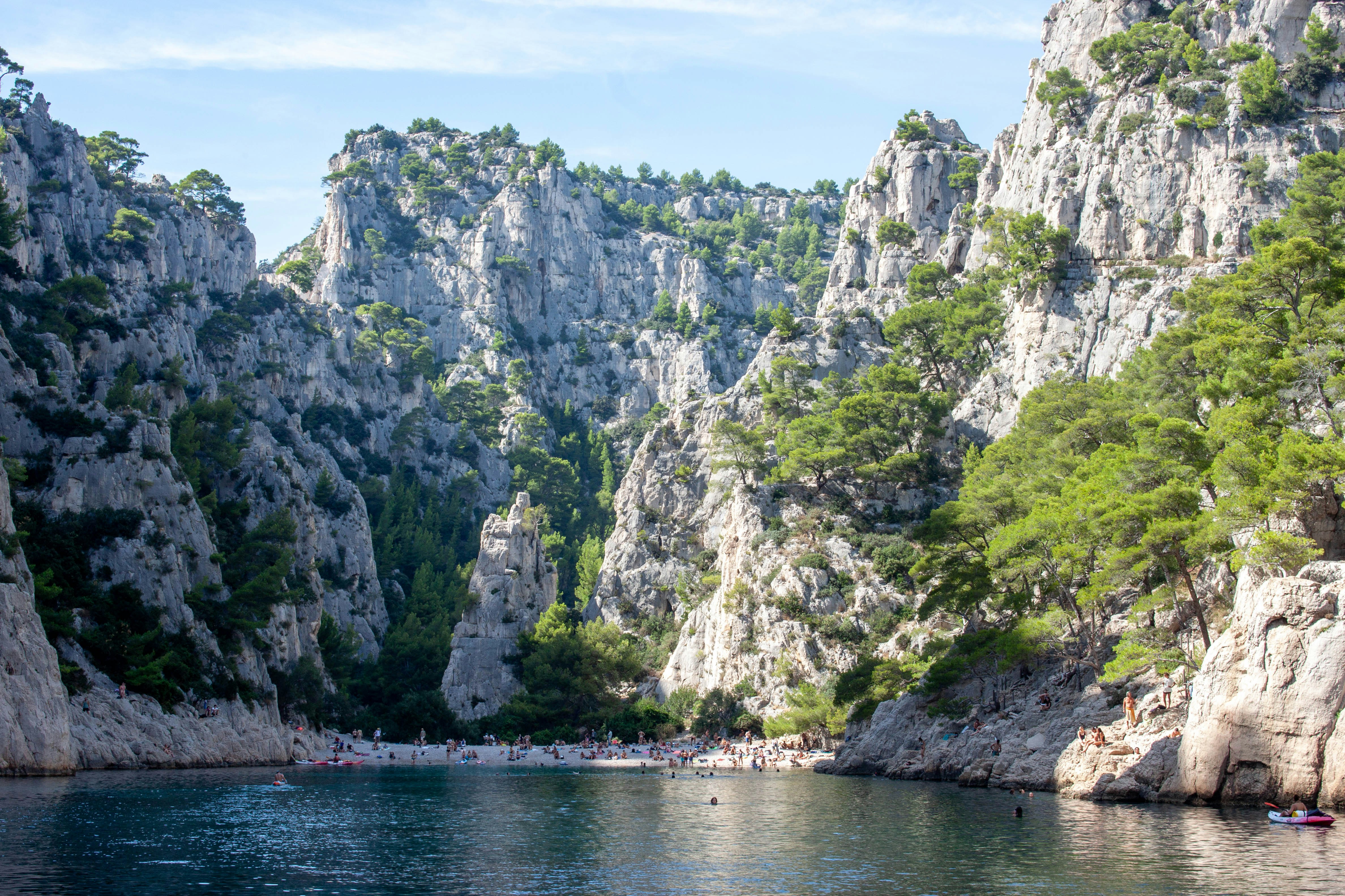 People on a small beach nestled between steep limestone cliffs and pine trees