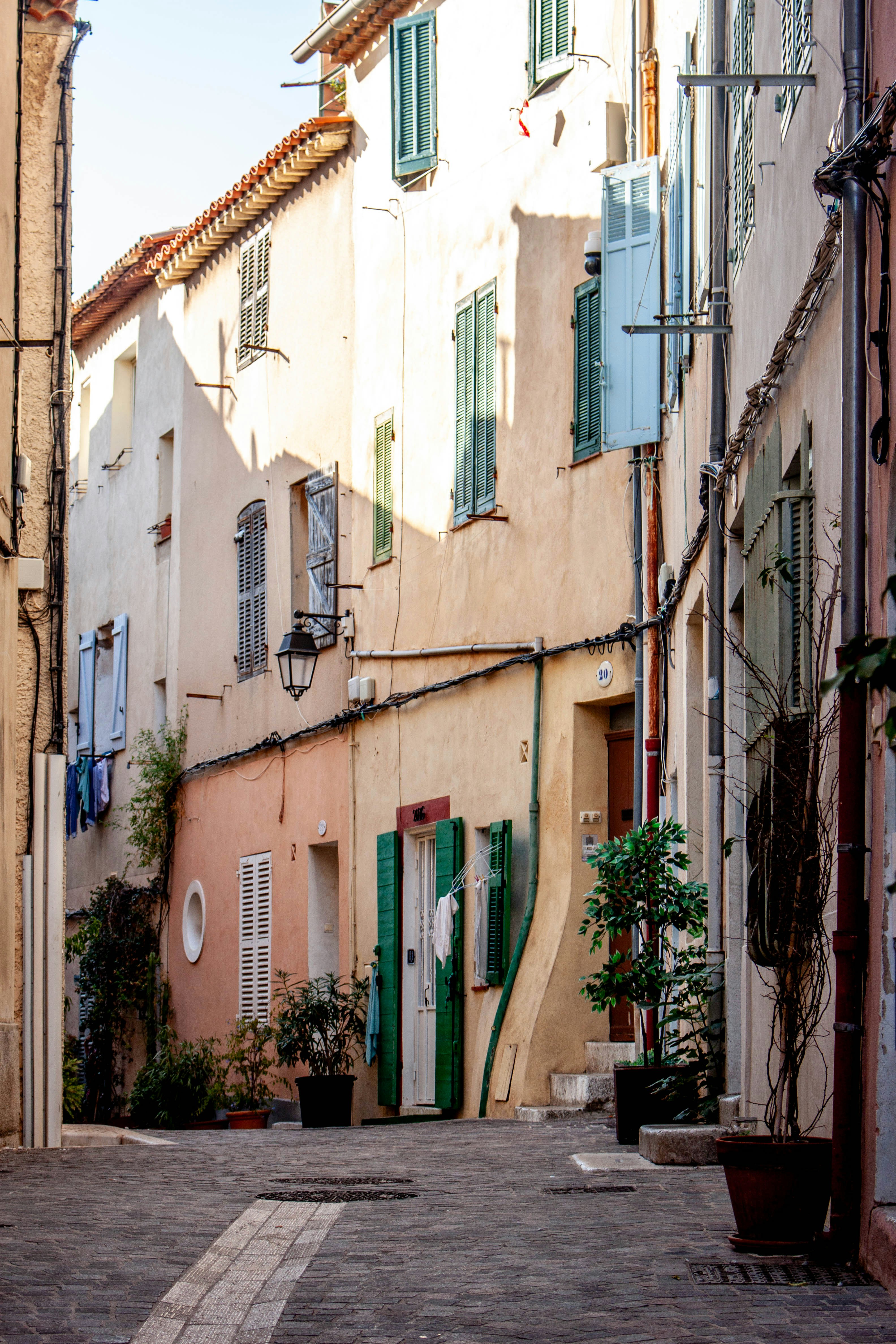 A narrow cobblestone street lined with tall pastel buildings and green shutters