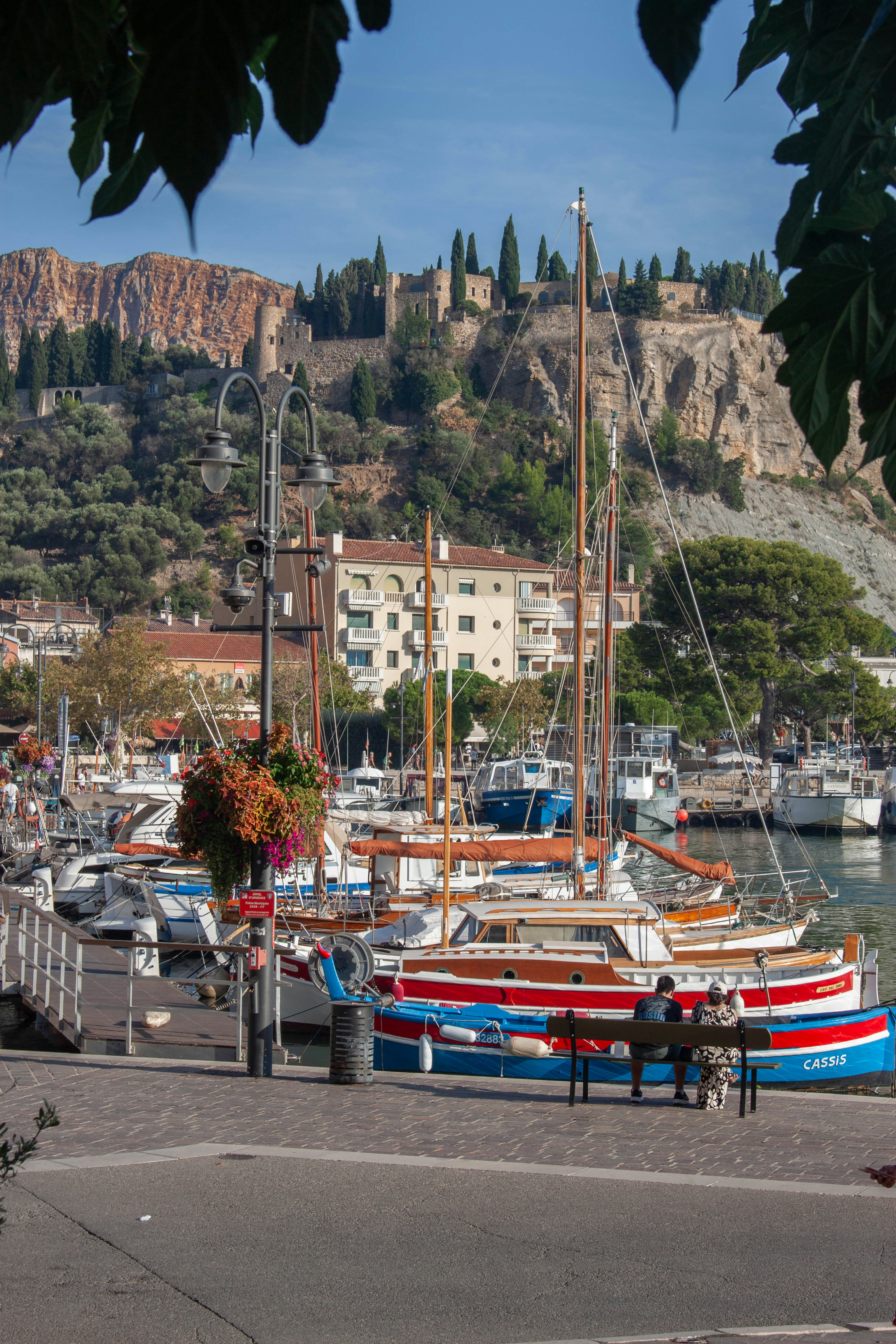 Two people sitting on a bench by boats in the harbor of Cassis