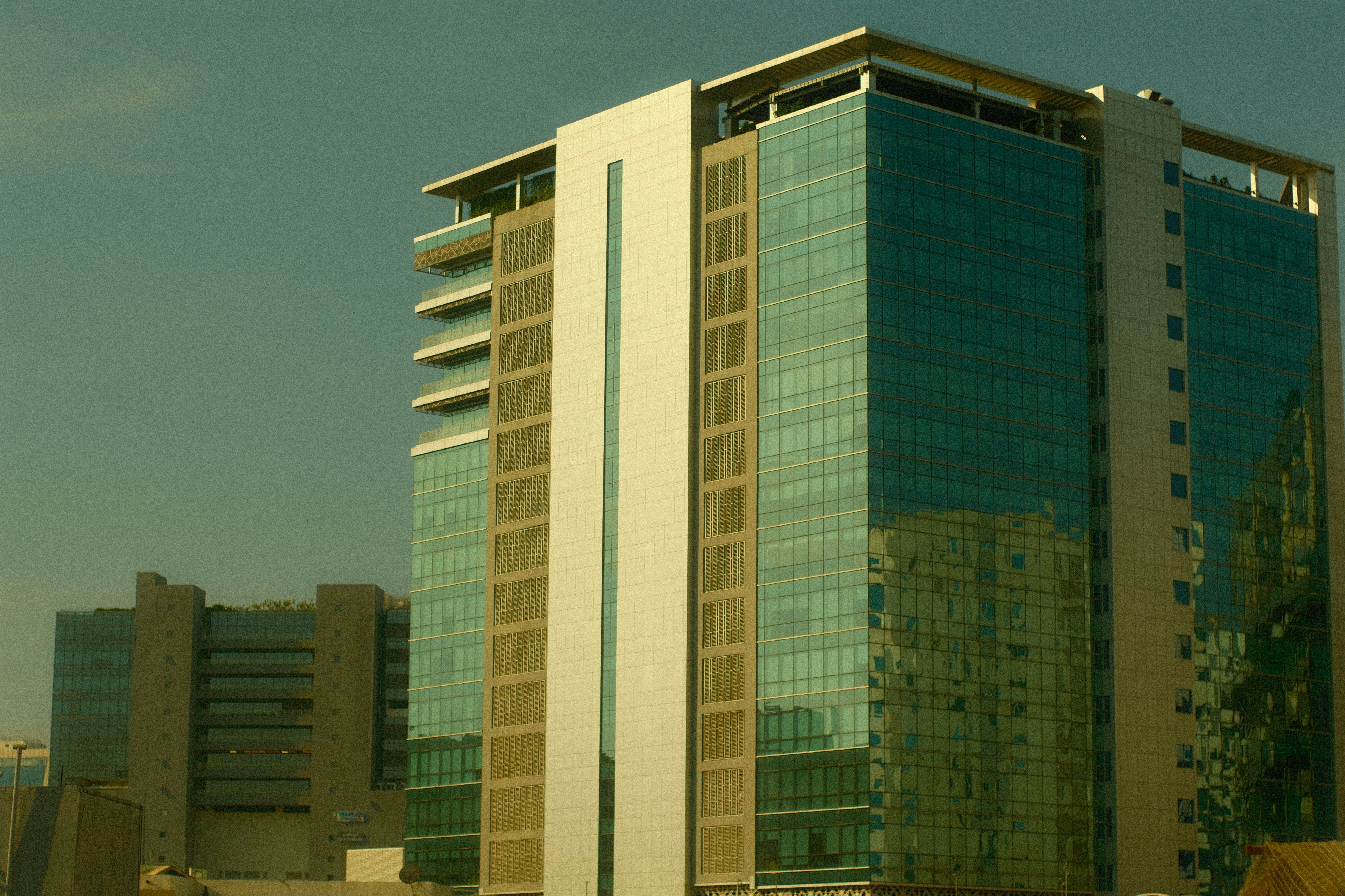 A modern glass office building with white panels against a clear sky