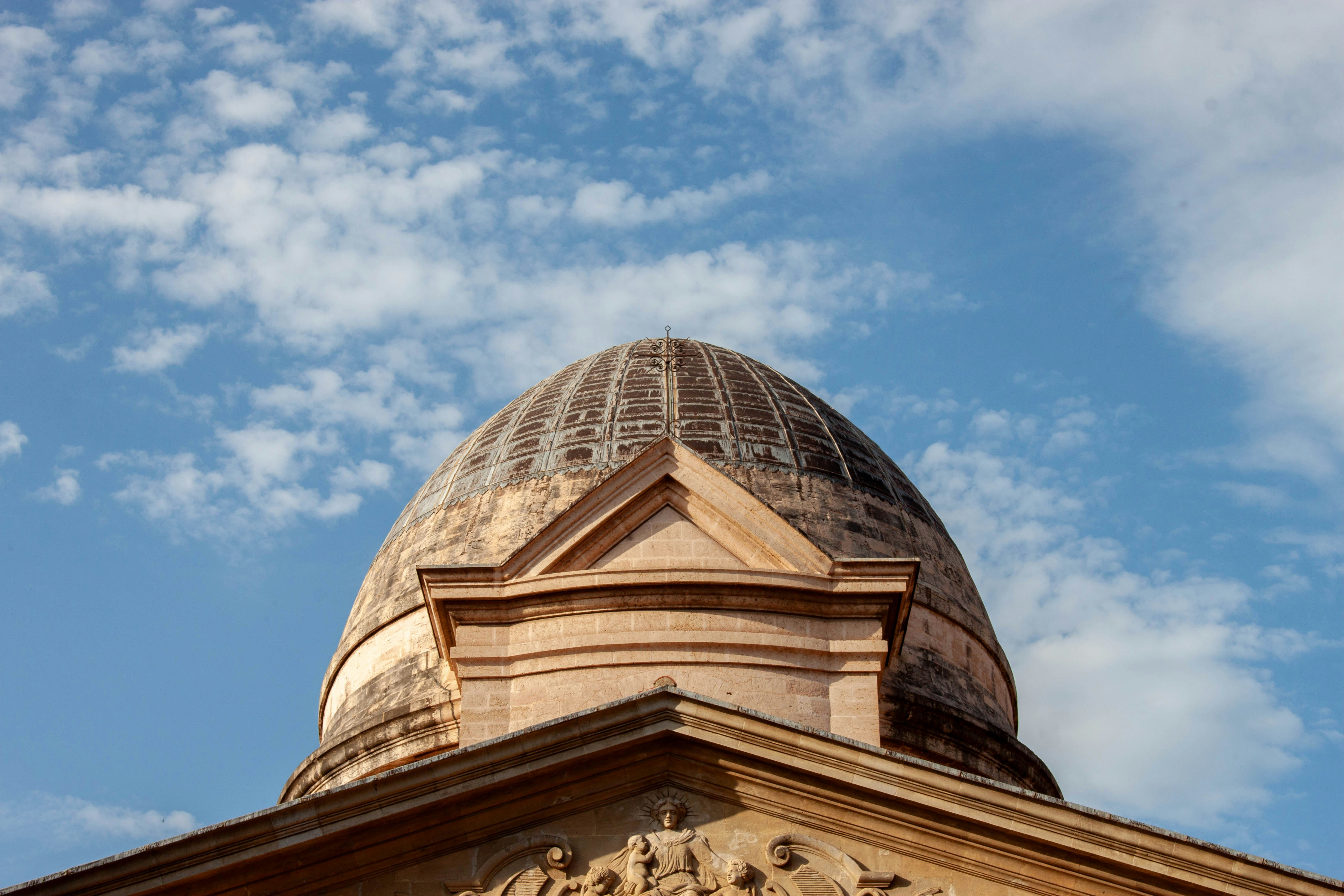 A stone dome with a cross against a blue sky with scattered clouds