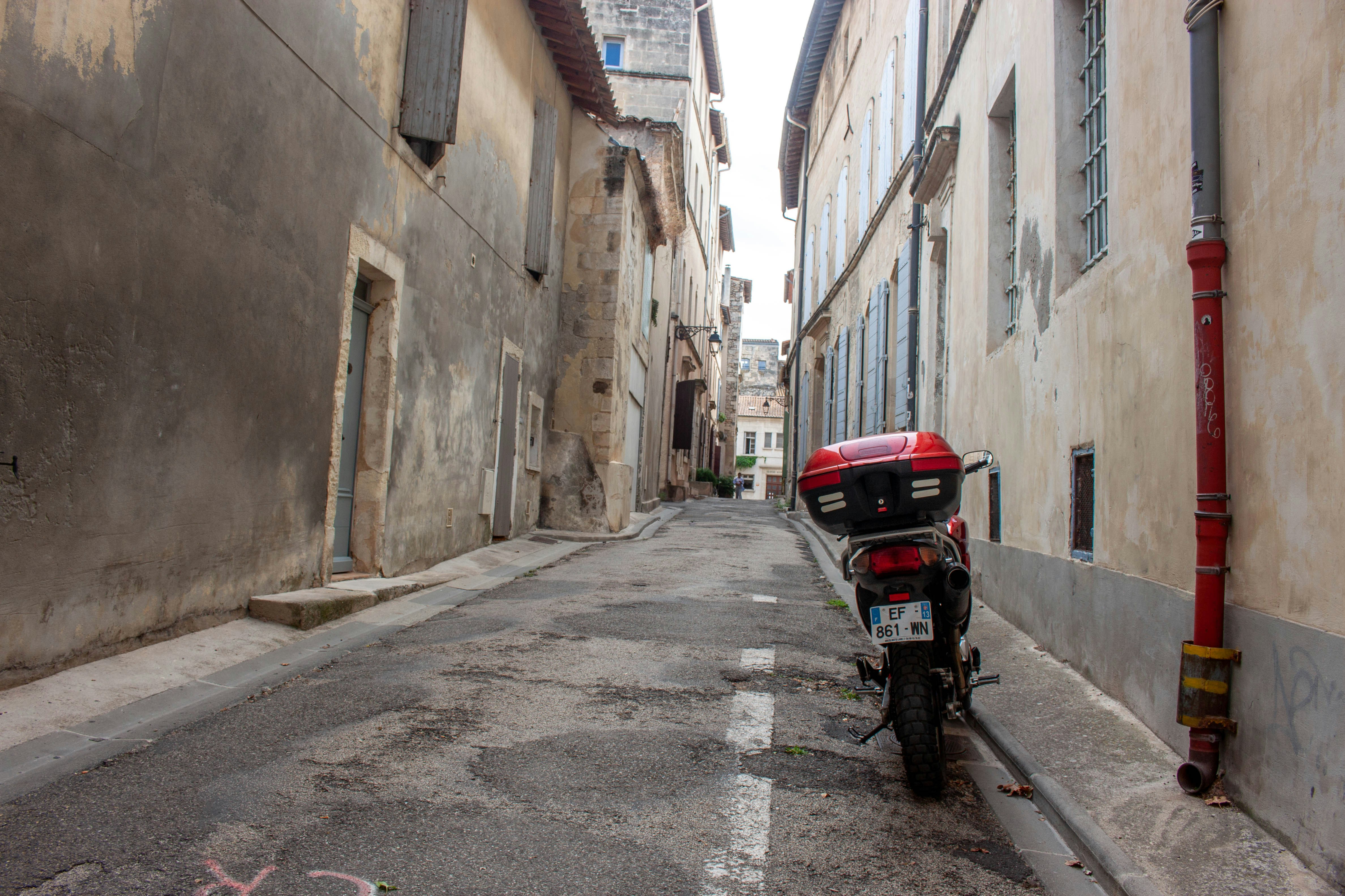 A red motorcycle parked in a narrow stone alleyway between old buildings