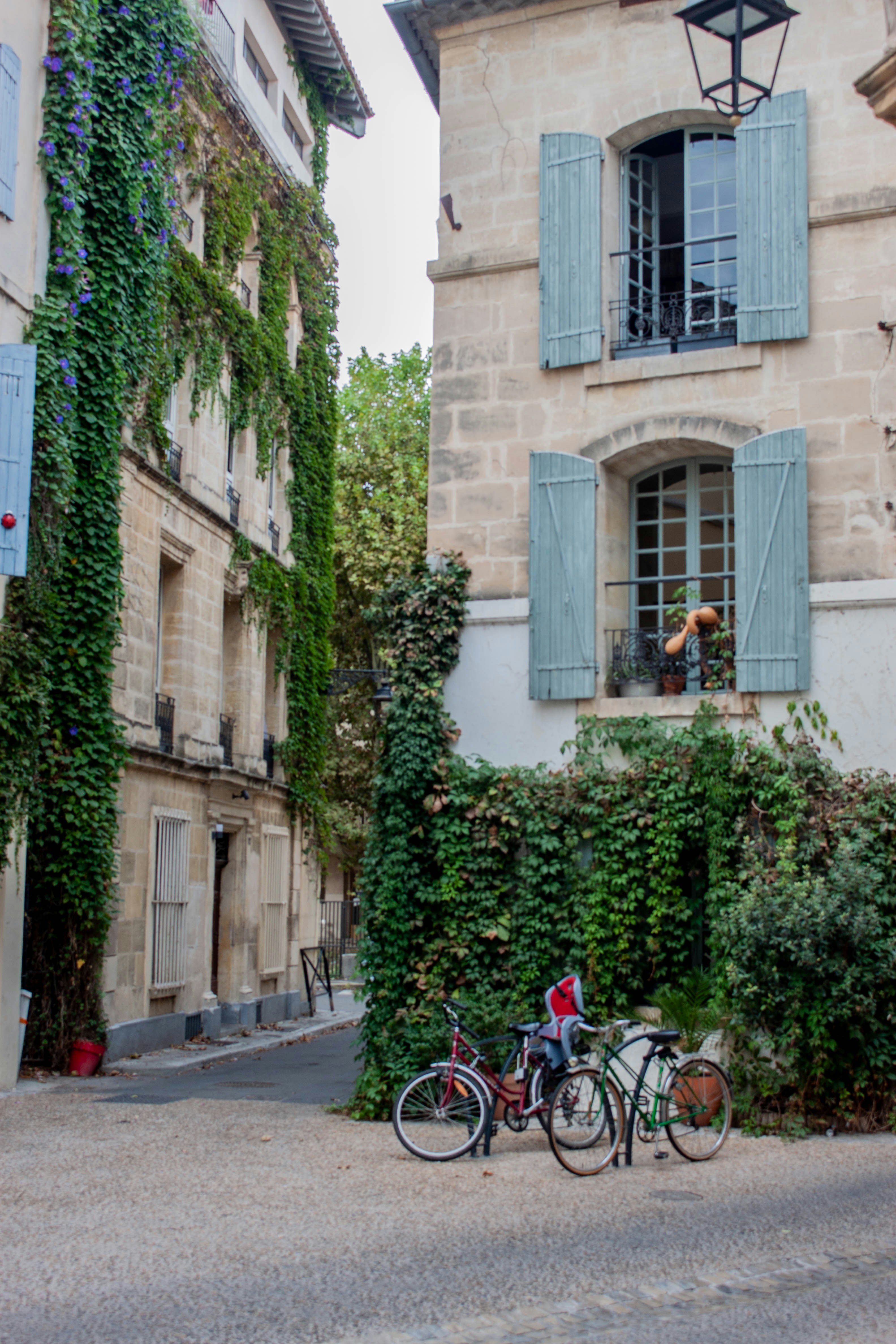 Two bicycles parked on a gravel path between stone buildings covered in ivy