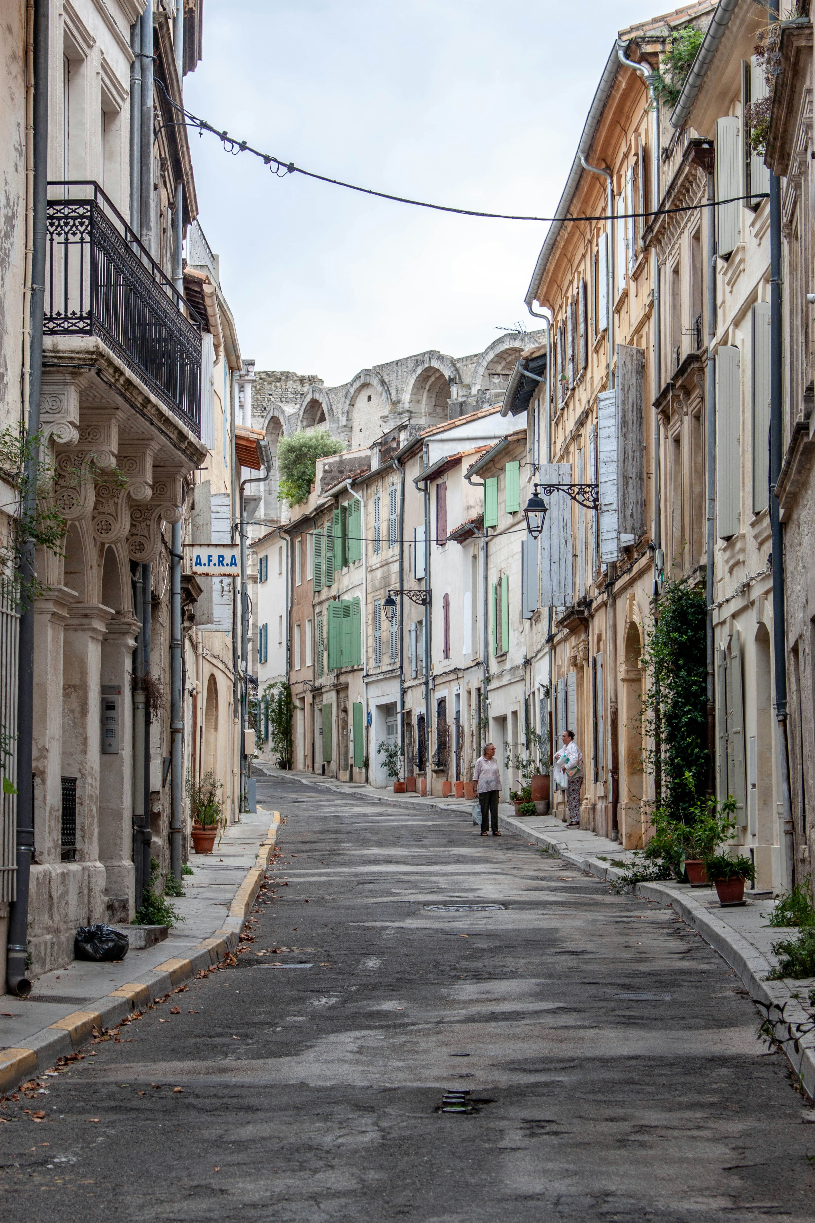 Two people on a narrow street lined with historic stone buildings in Arles