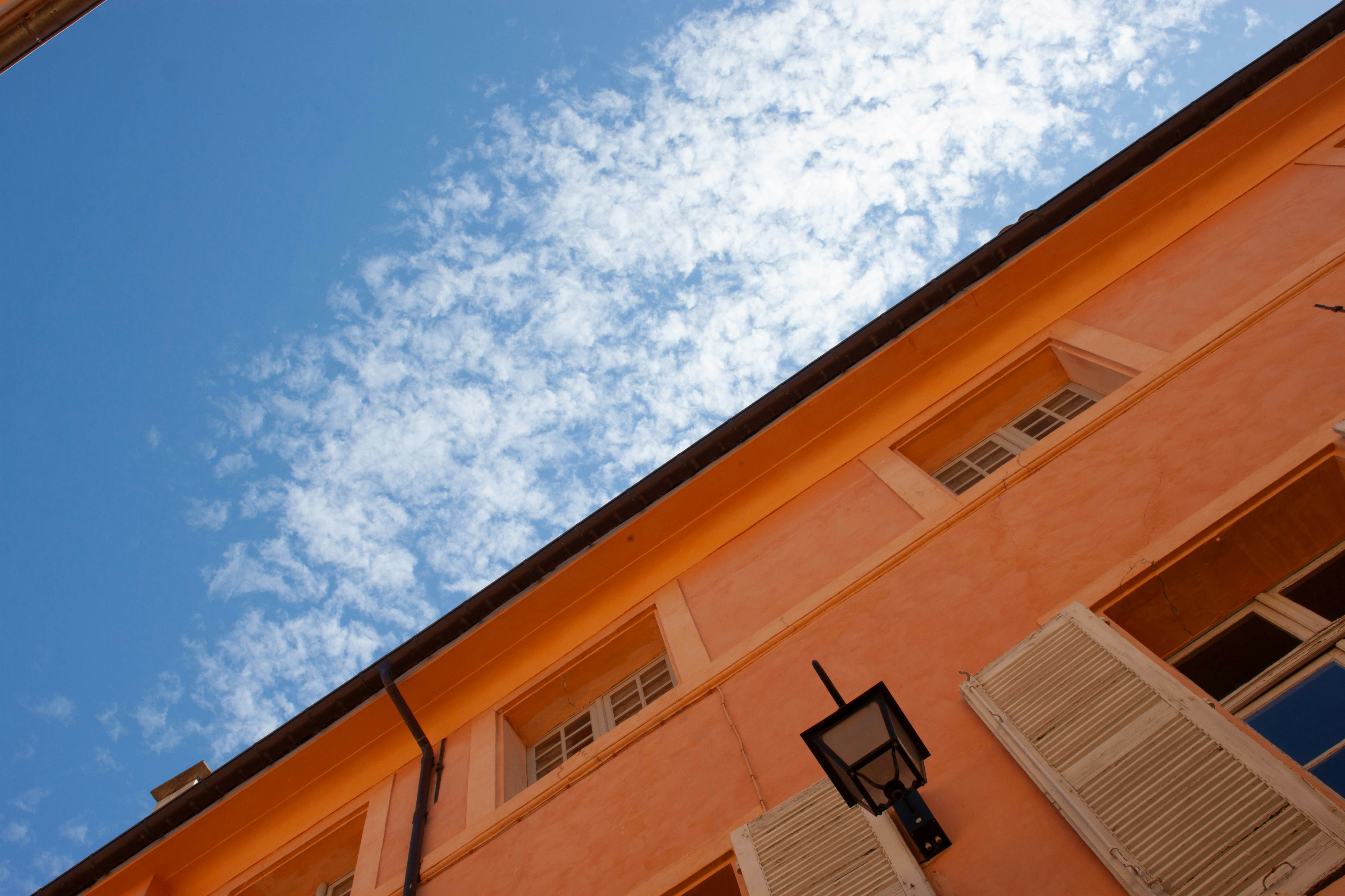 Une façade orange avec des volets blancs sous un ciel bleu vif