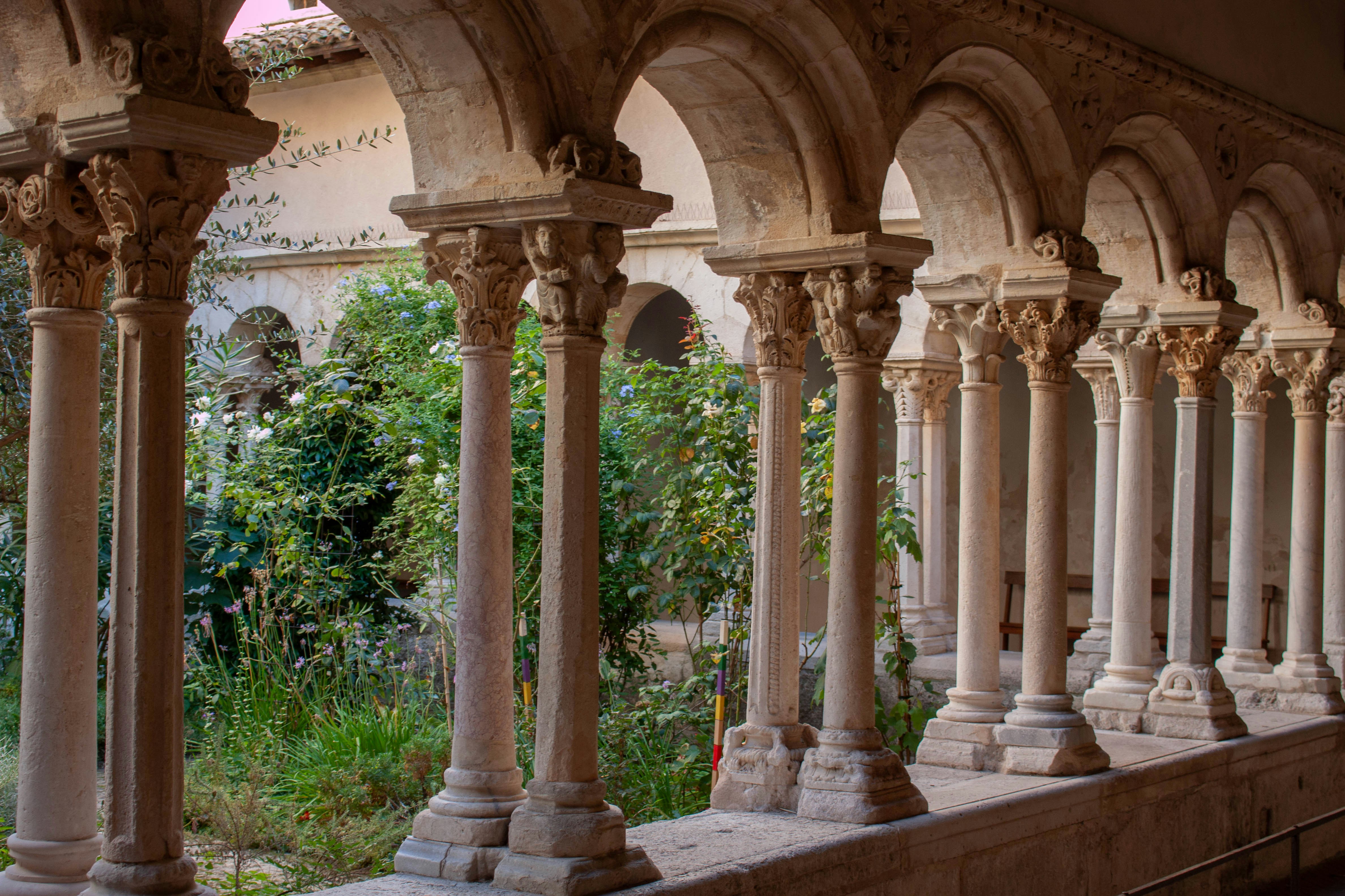 Stone columns with carved capitals lining a cloister walkway beside a lush garden