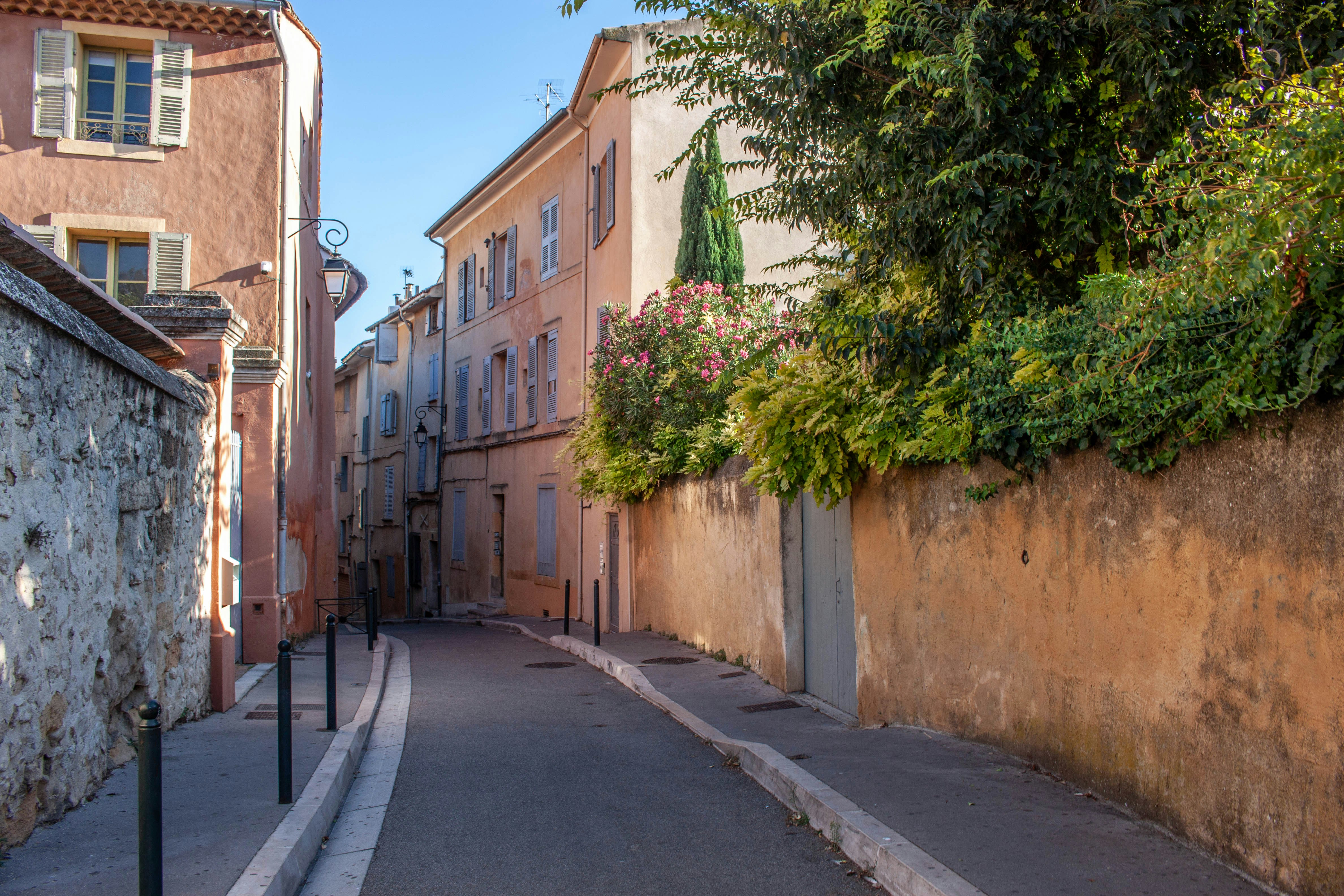 A narrow street between tall peach-colored buildings with green shutters and stone walls