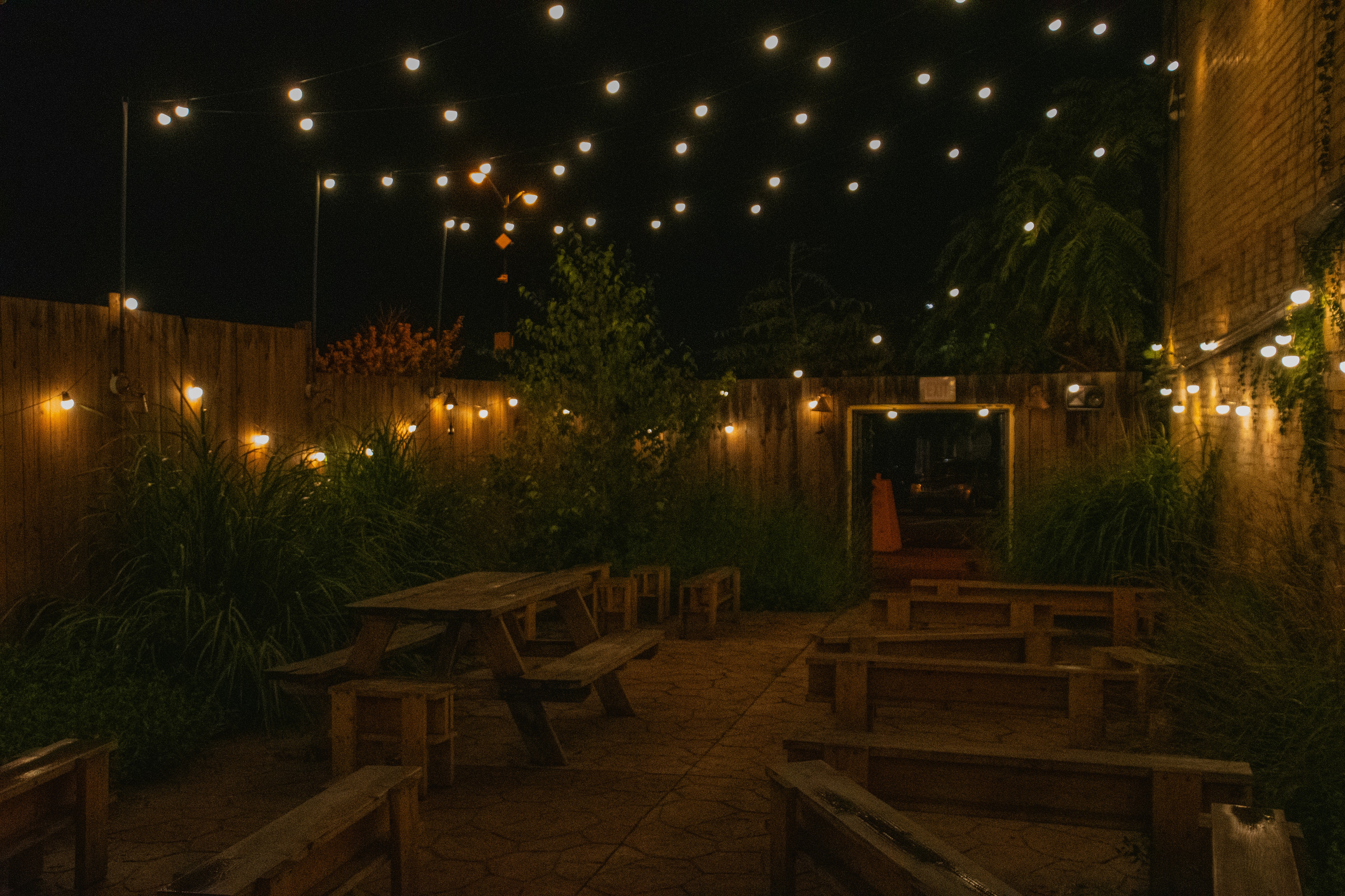 Mesas y bancos de madera en un patio iluminado con guirnaldas de luces por la noche