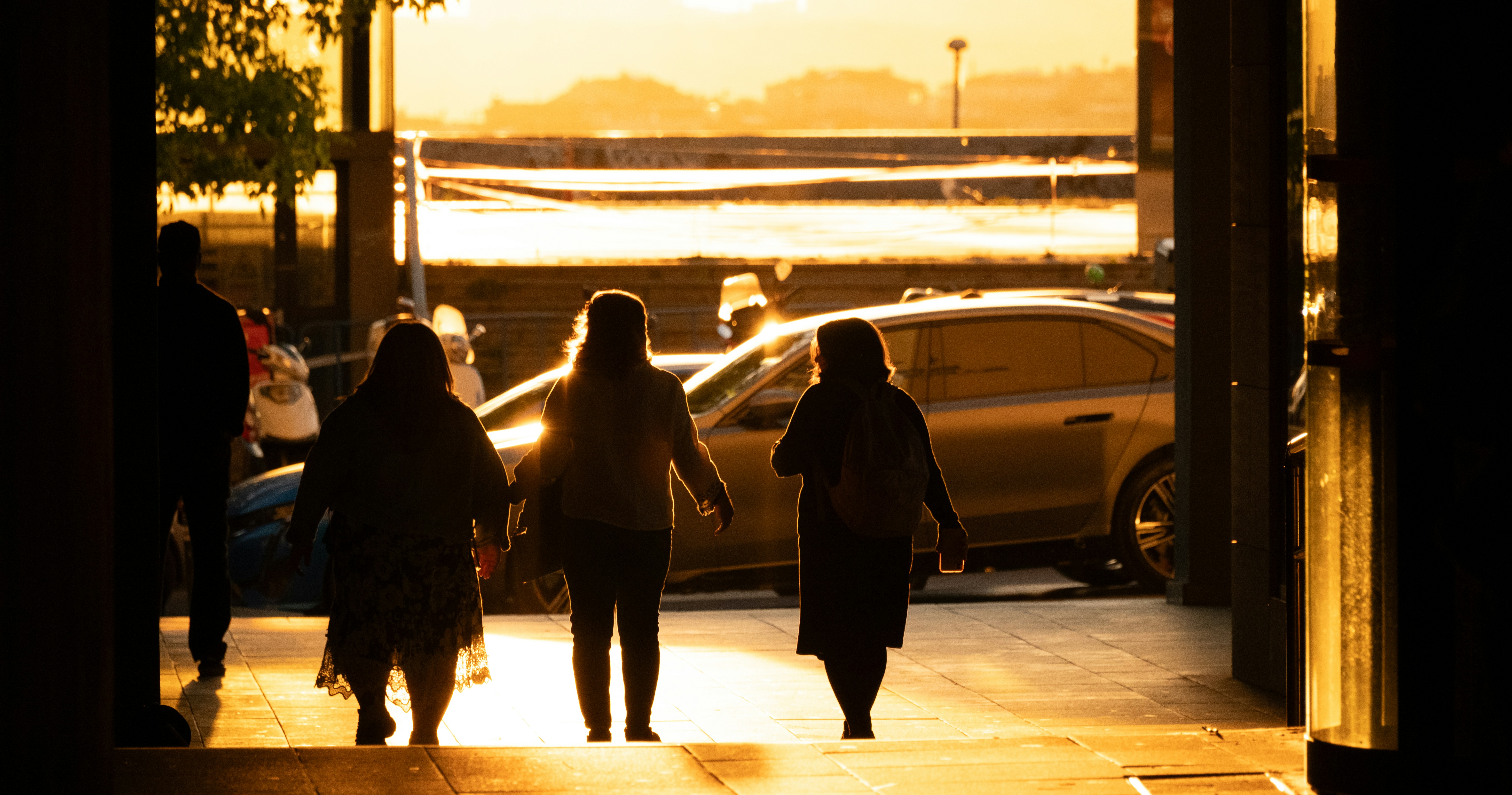 Silhouettes of four people walking on a city sidewalk during golden hour