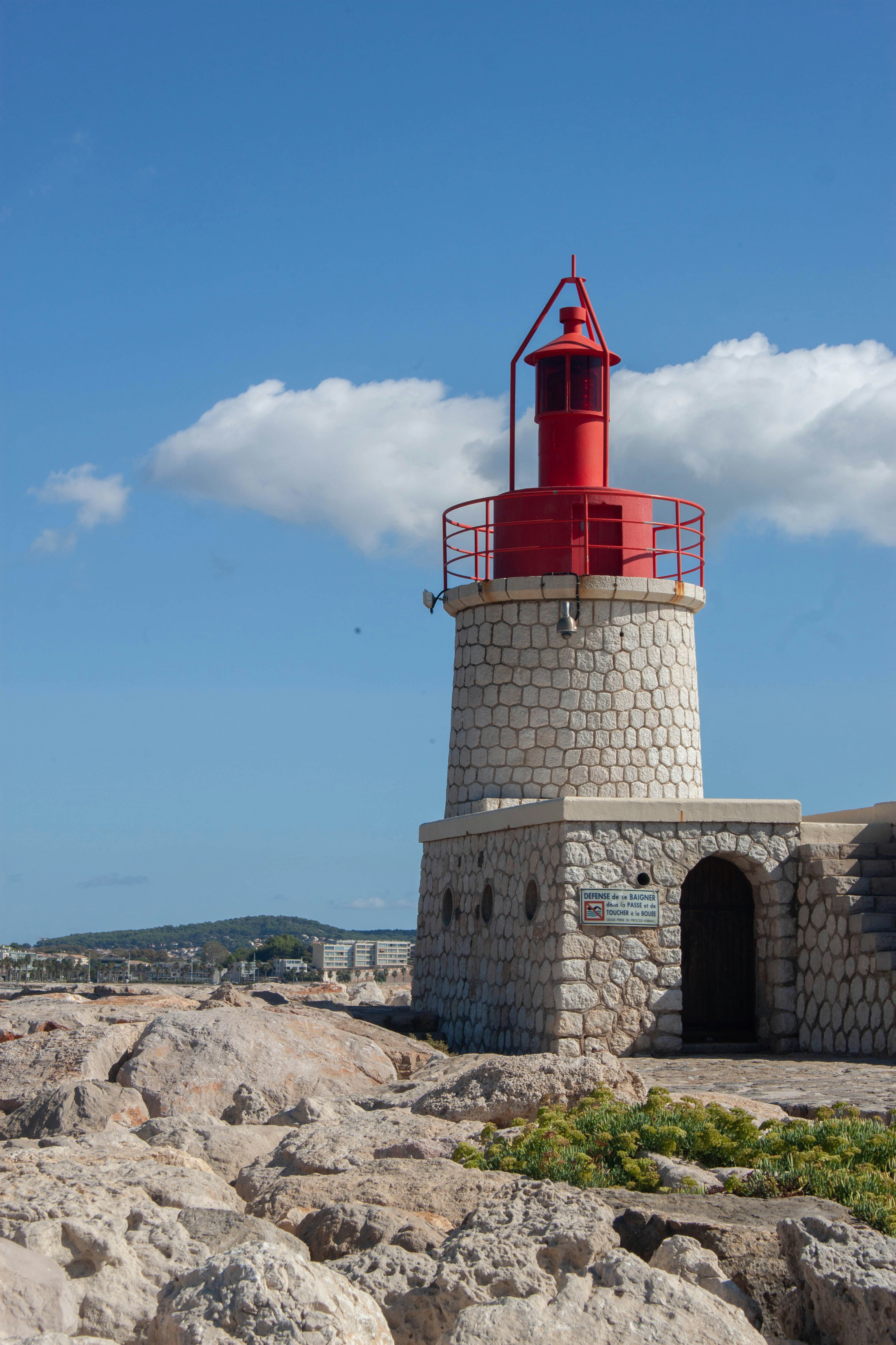 A stone lighthouse with a red lantern room on a rocky coastal breakwater