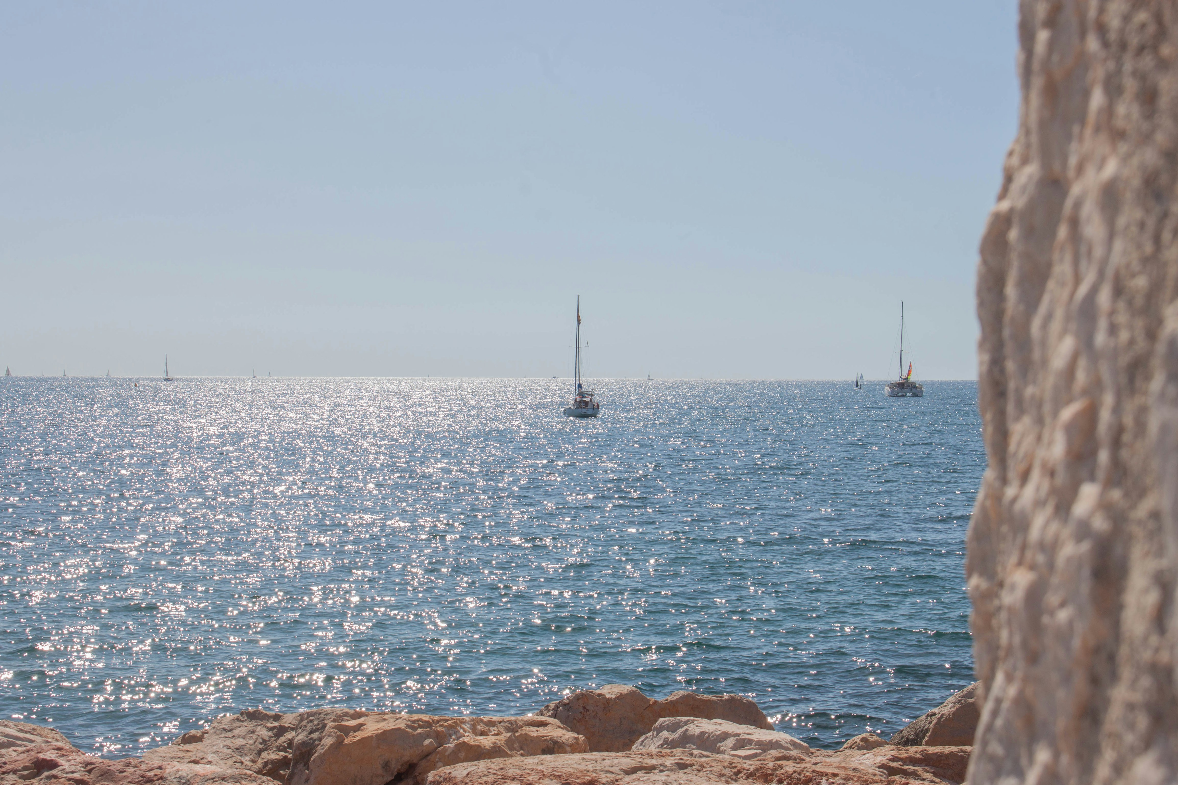Barche a vela sul mare azzurro scintillante viste da una costa rocciosa